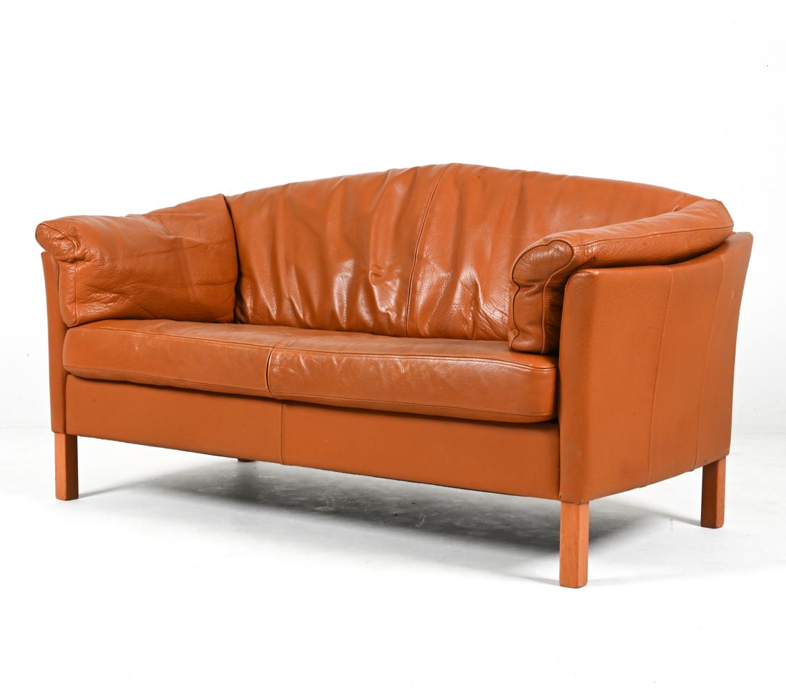 This iconic model 535 two-seat sofa by Mogens Hansen features slightly bowed shelter arms and comfortable plush cushions atop sturdy oak legs. The upholstery is a handsomely patinated tan leather - reminiscent of an English saddle - with accent