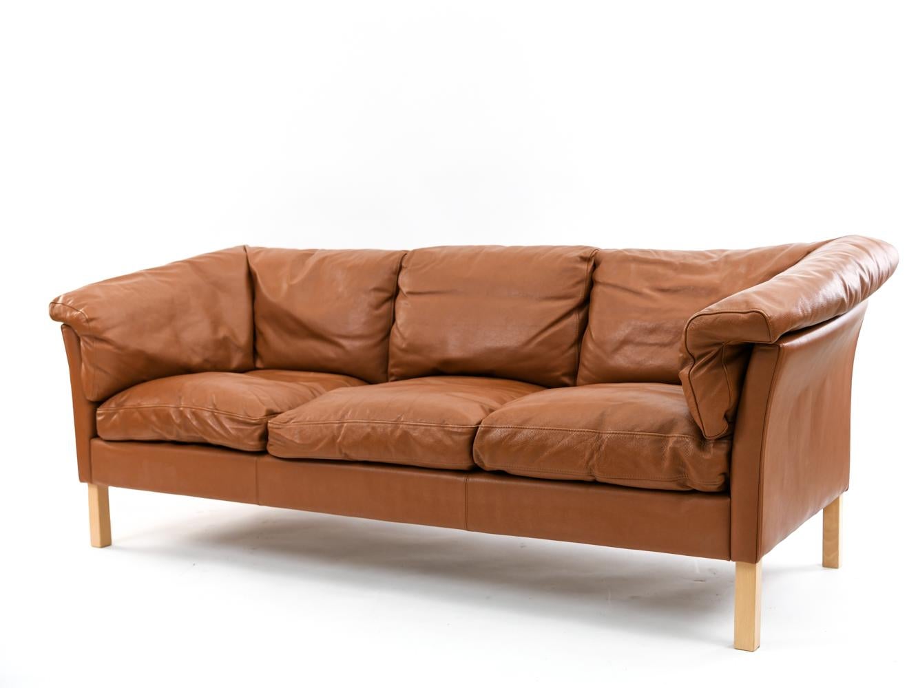 This Danish midcentury sofa suite by Mogens Hansen features a three-seat sofa and two-seat loveseat upholstered in soft, comfortable brandy colored leather. Use this set as a wonderful way to fill a space creating a cohesive, unified and modern