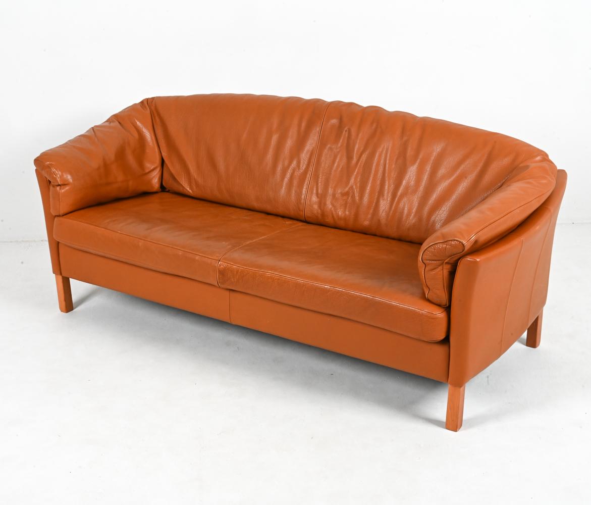 This iconic model 535 three-seat sofa by Mogens Hansen features slightly bowed shelter arms and comfortable plush cushions atop sturdy oak legs. The upholstery is a handsomely patinated tan leather - reminiscent of an English saddle - with accent