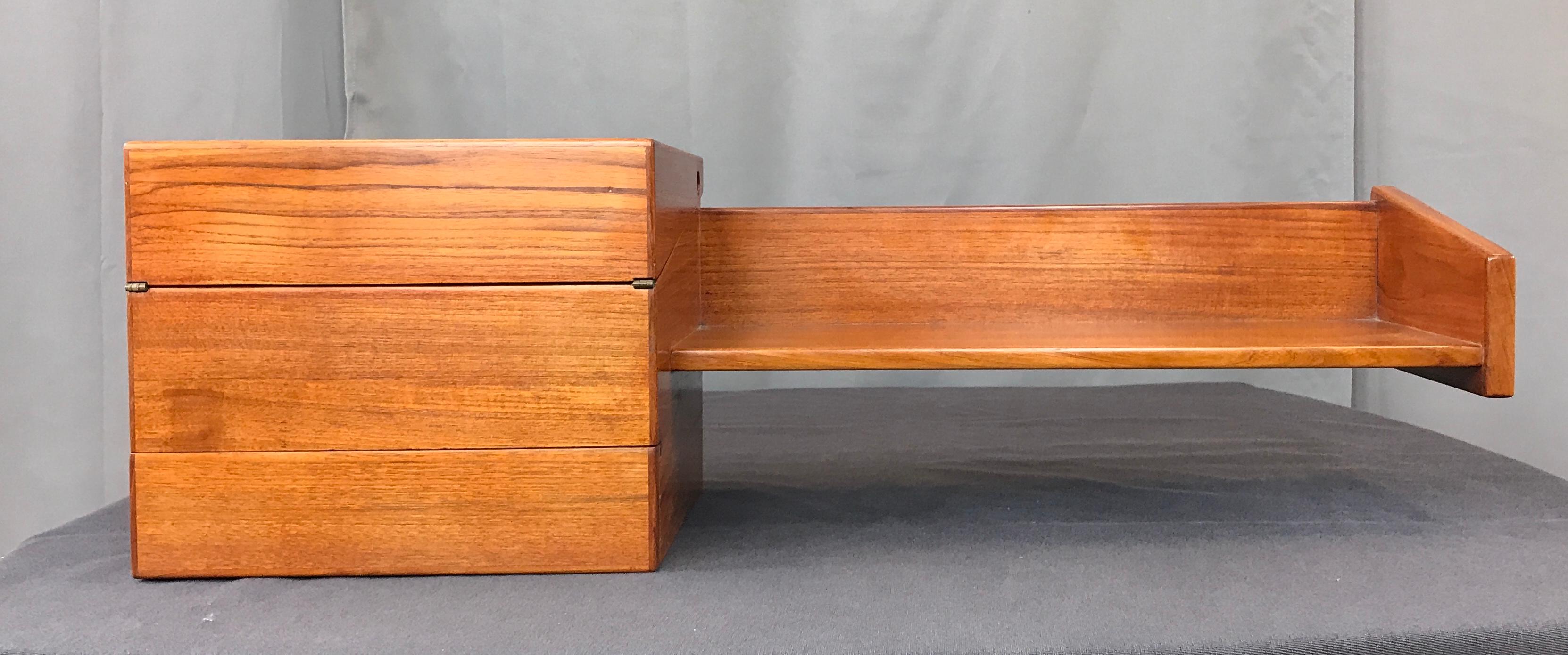 A Mogens Kold Teak floating shelf and desk, made in Denmark. A floating shelf on the right, attached to it on the left, a cube, with a drawer on the bottom. Top half flips over to reveal a chamber, with the lid that can be use as a small desk,