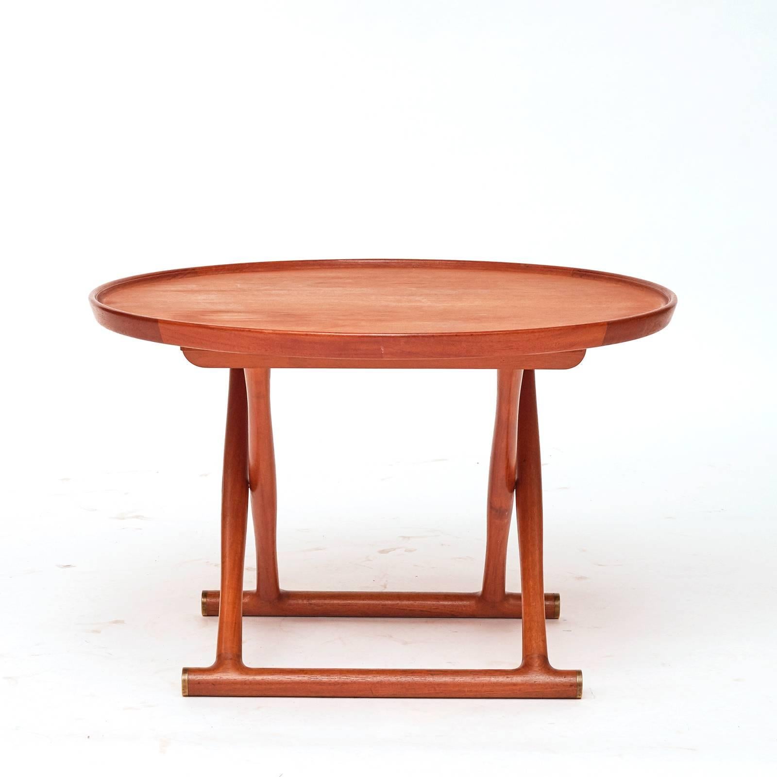 A Classic Danish modern teak wood and brass folding circular table, aptly named the Egyptian table due to the ancient form. The circular folding lipped top above cross-supports ending with concave brass caps. The design of this table was from 1954.