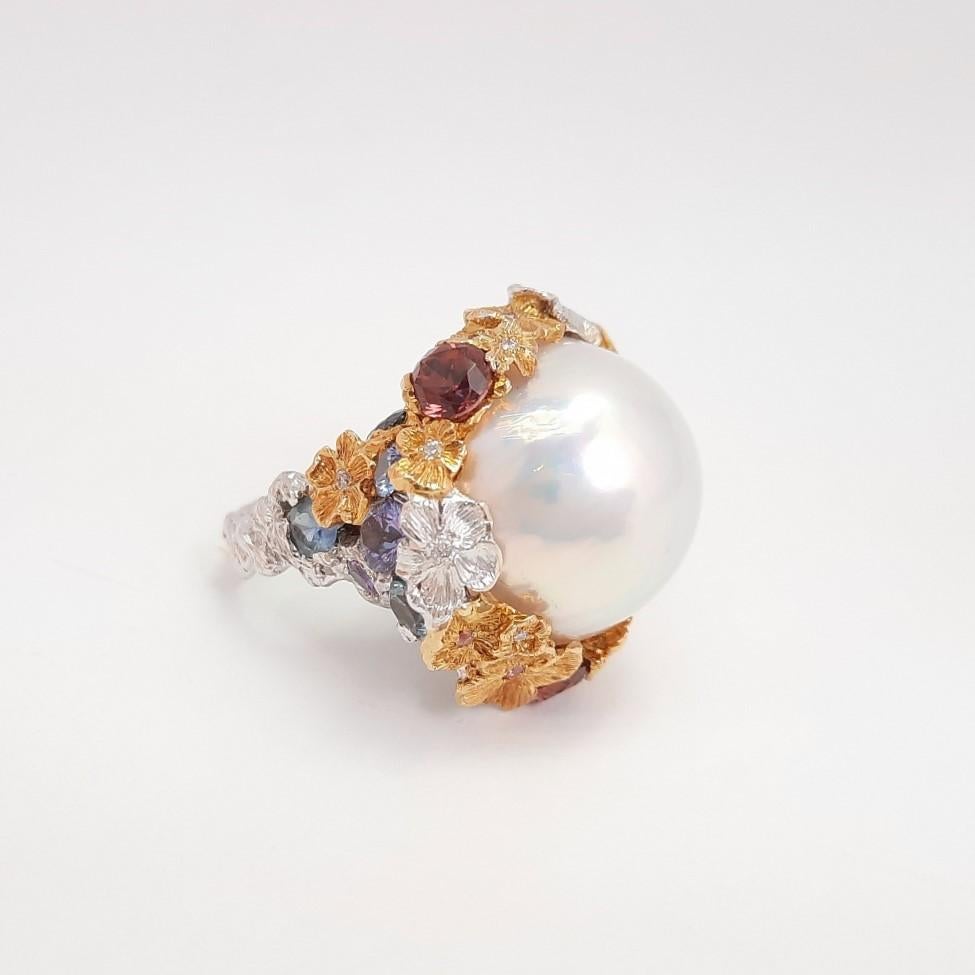 20mm size breath-takingly beautiful Mabe Pearl is artistically mounted in tender flower design decorated with multiple colour sapphires. The shimmer with a rainbow effect captures your eyes while  comforting your mood. The tree branch-like gold