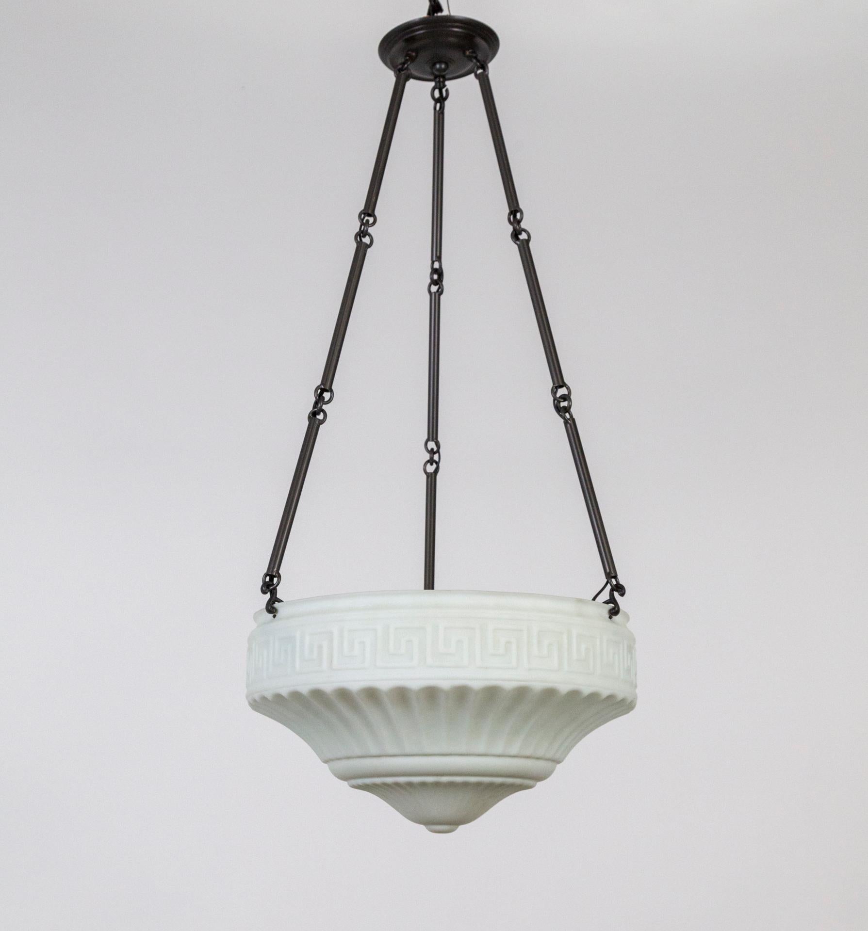 An Art Deco, molded, matte milk glass shade; etched with a Greek key motif and shaped with decorative grooves in a radial form. Three black tinted brass stems hold it to the canopy. 3 medium base sockets. Measures: 35.5” height x 16” diameter.