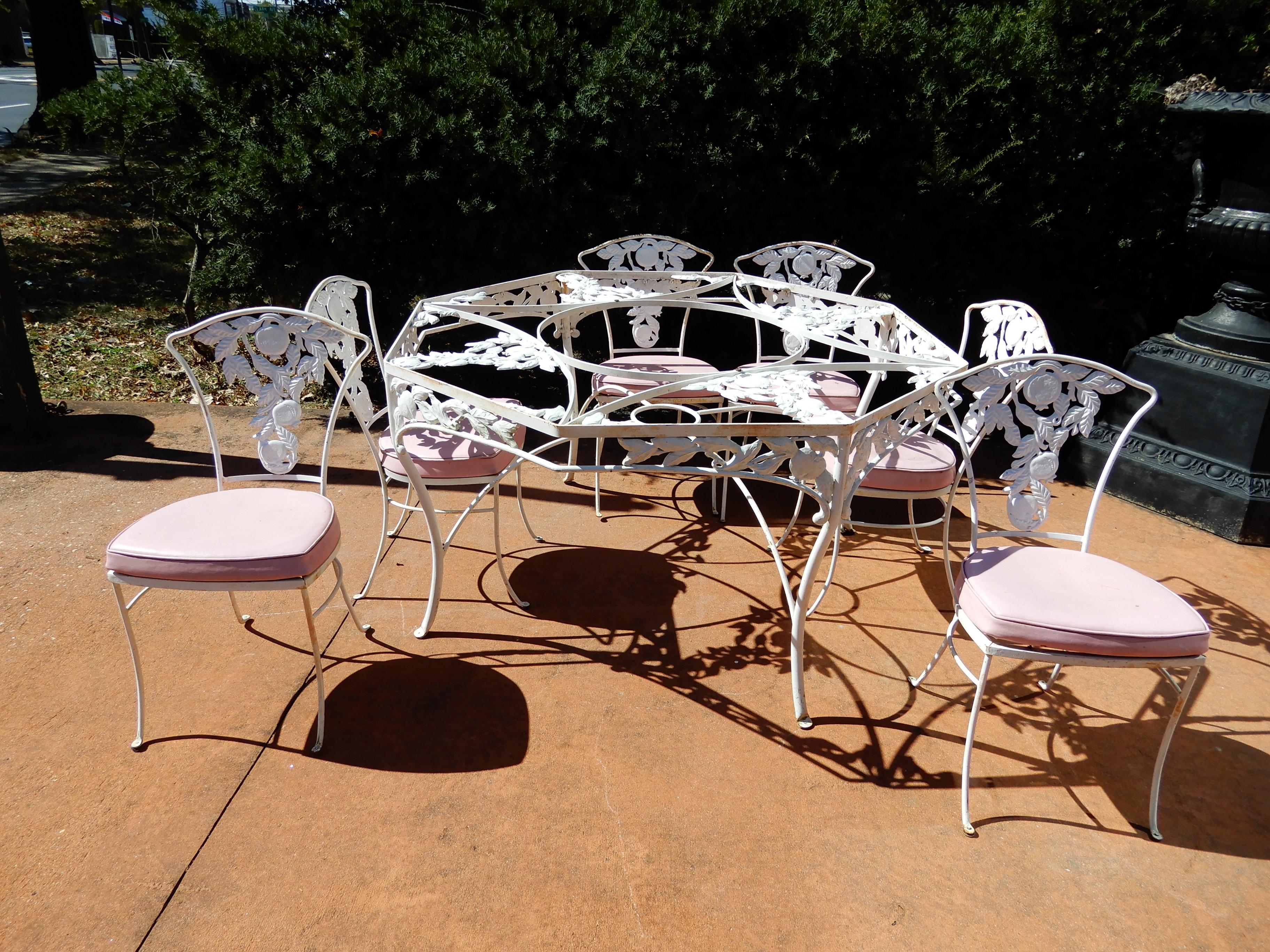 An elaborate cast aluminum dining set in the pomegranate pattern. The table in an octagonal shape and chairs with pomegranates. The set with original pink vinyl seat cushions that exhibit wear.
 