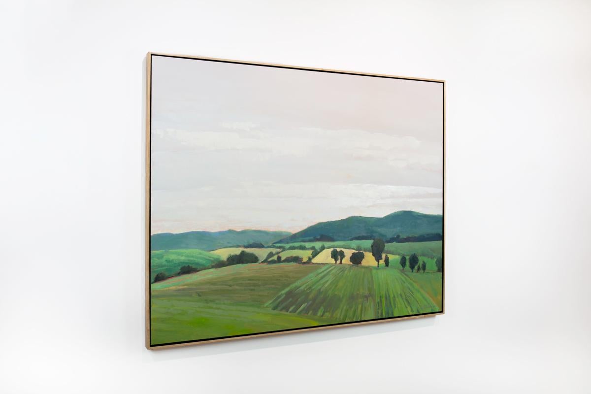 This traditional landscape painting by Molly Doe Wensberg features a cool palette, and captures a lightly abstracted scene of lush green, rolling hills under a pale sky. The painting is made with oil paint on gallery wrapped canvas, which is framed