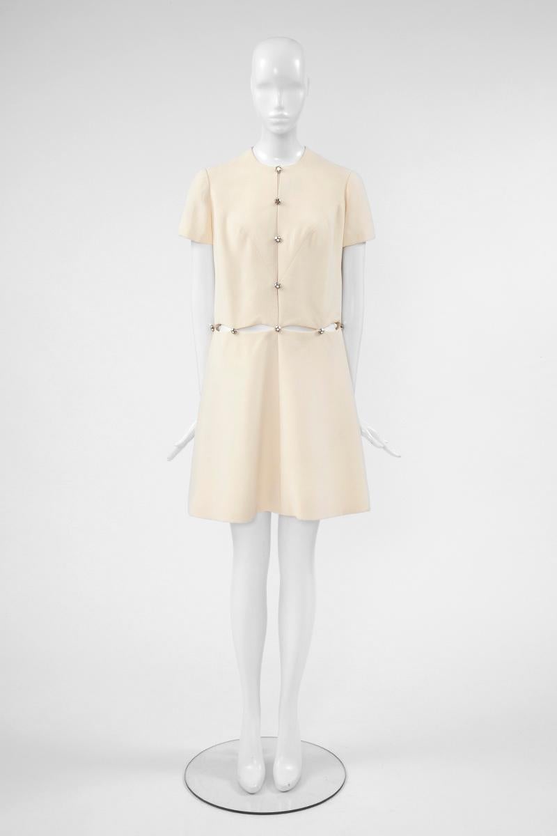 A wonderful and chic 60’s dress by the famous French couture house Molyneux. Constructed in off-white coloured wool, this dress features a round neckline, short sleeves and a slight drop-waist silhouette. Bold cut-outs are to be found along the bust