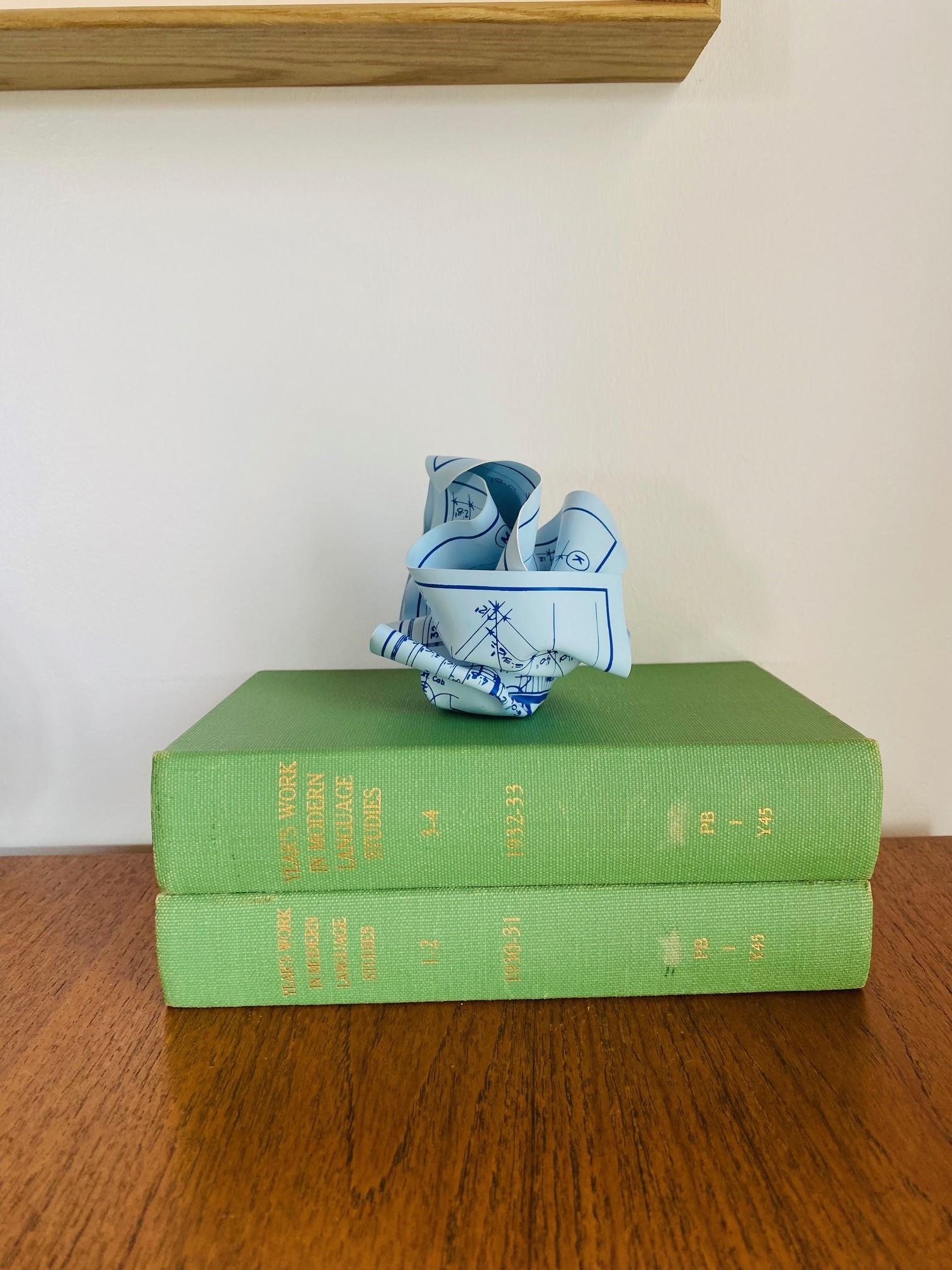 This three-dimensional art object, which can also be a practical desktop paperweight, was designed by Tibor Kalman. It's made of rigid silk-screened vinyl featuring a replica of an architectural drawing, hand-crumpled, and wrapped around a steel