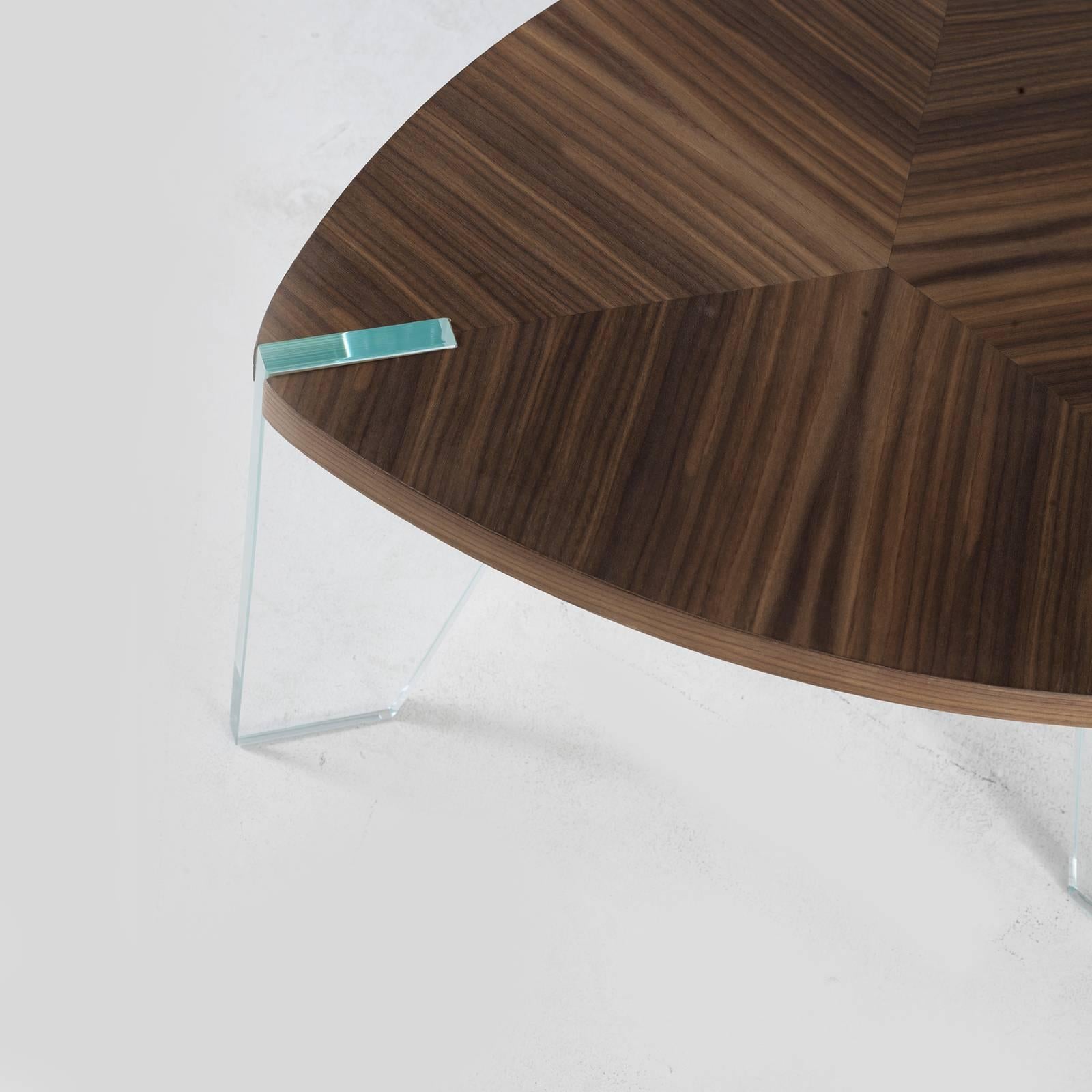 The walnut triangular top with rounded corners of this captivating coffee table becomes a lightweight shelf when supported by three extra-clear tempered glass legs. The surface is enhanced by the wood grain and an elegant herringbone pattern and