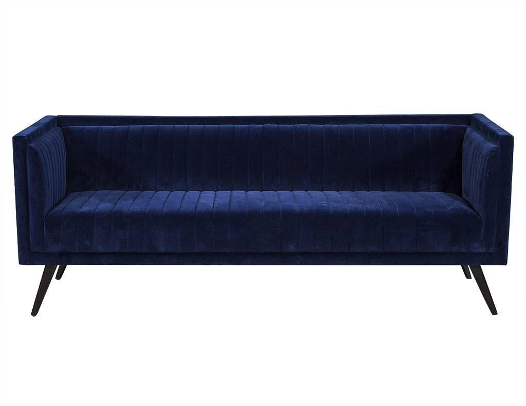 This modern sofa is made to order. Coated in a deep blue fabric, it sits atop angled and tapered dark finished legs. Although the blue is luxurious, there are other upholstery options available so please inquire for pricing. A perfect fit for a