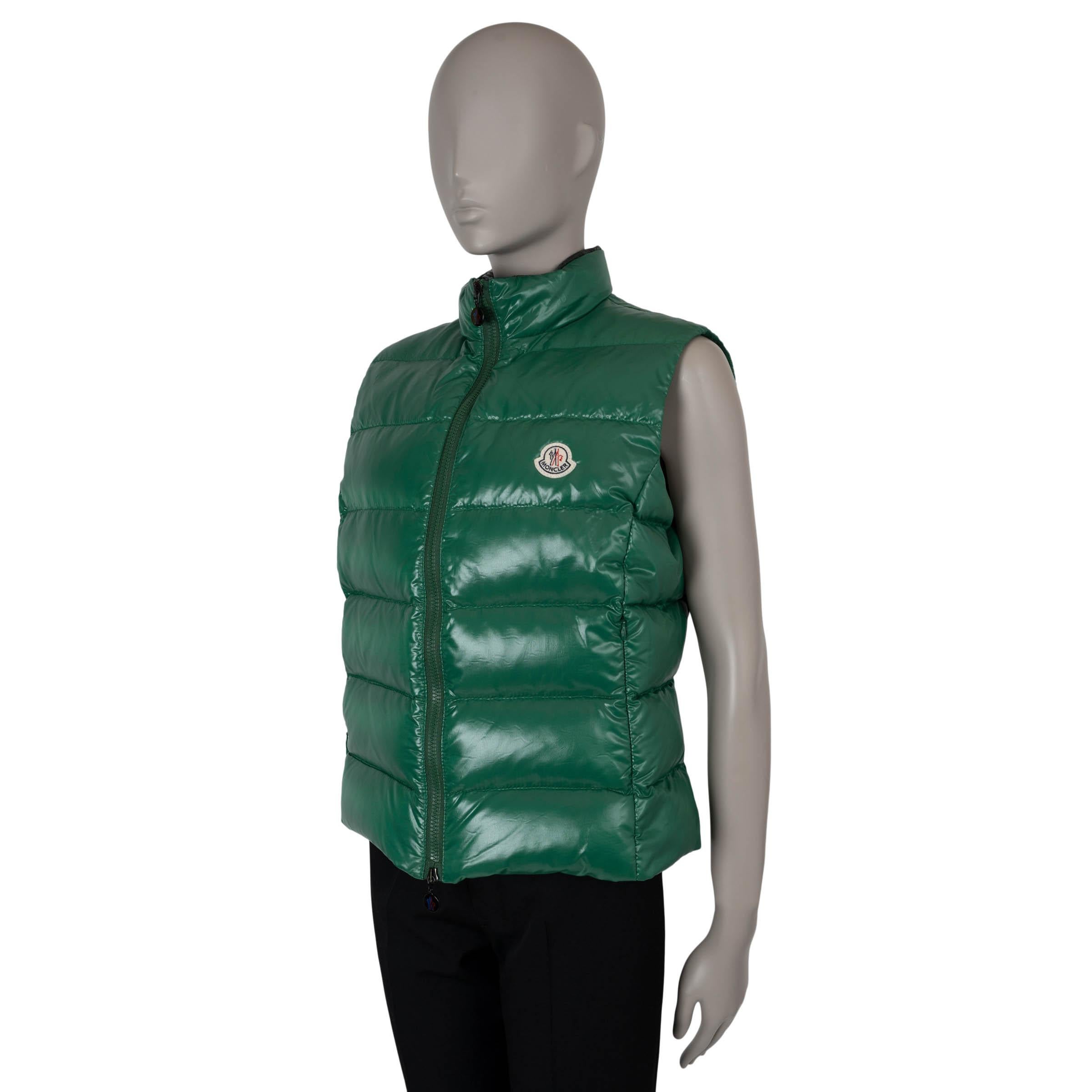 This 100% authentic Moncler Ghany puffer vest in dark green quilted shiny nylon laqué offers a sleek, fitted silhouette with a high collar and convenient zip pockets at the waist. It closes with a front zipper and is lined in polyamide (100%) with