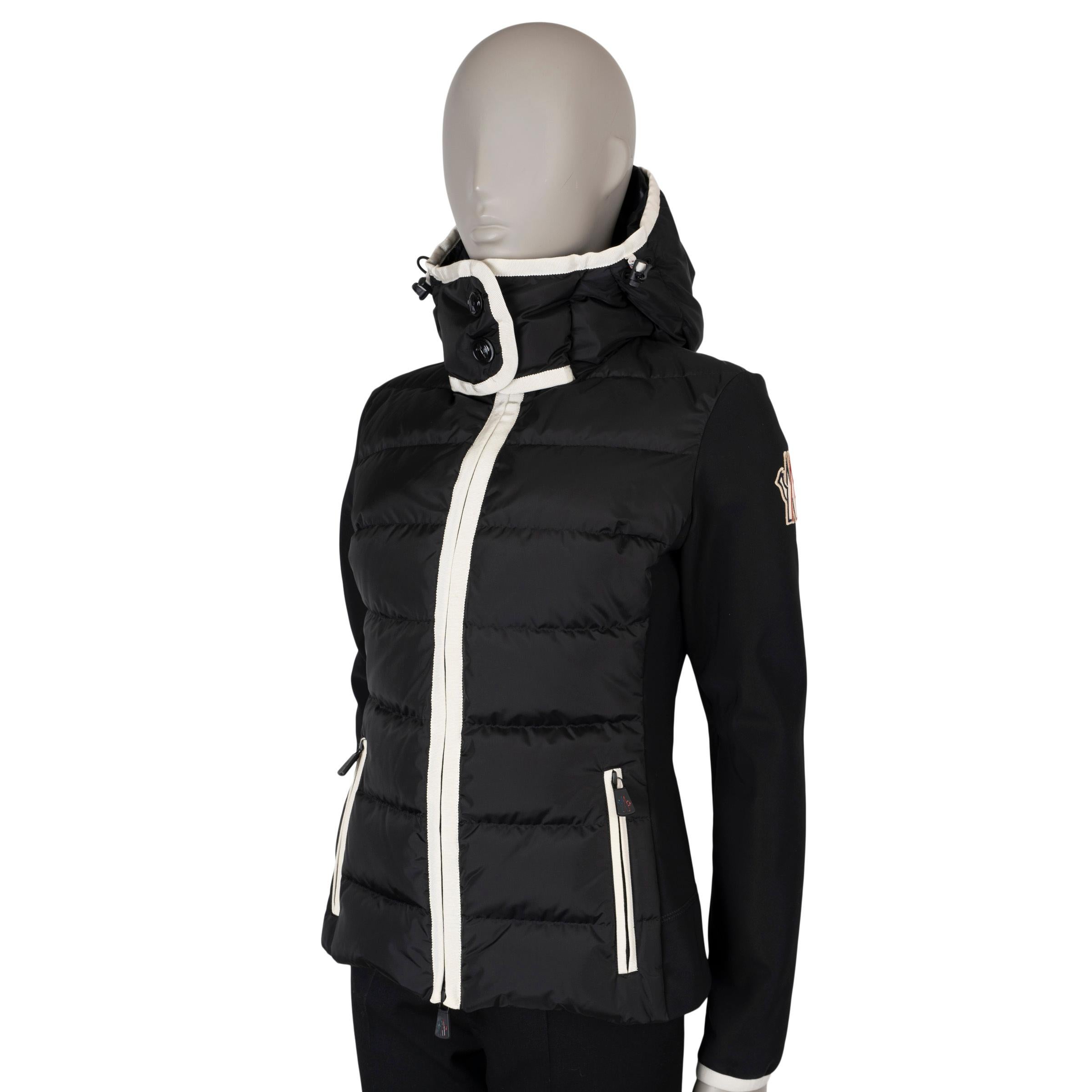This 100% authentic Moncler Grenoble Maglia zip-up cardigan in black performance fleece with a down-filled nylon front is perfect as a mid-layer or outerwear in milder weather. It features contrasting white trims, an adjustable drawstring hood, and