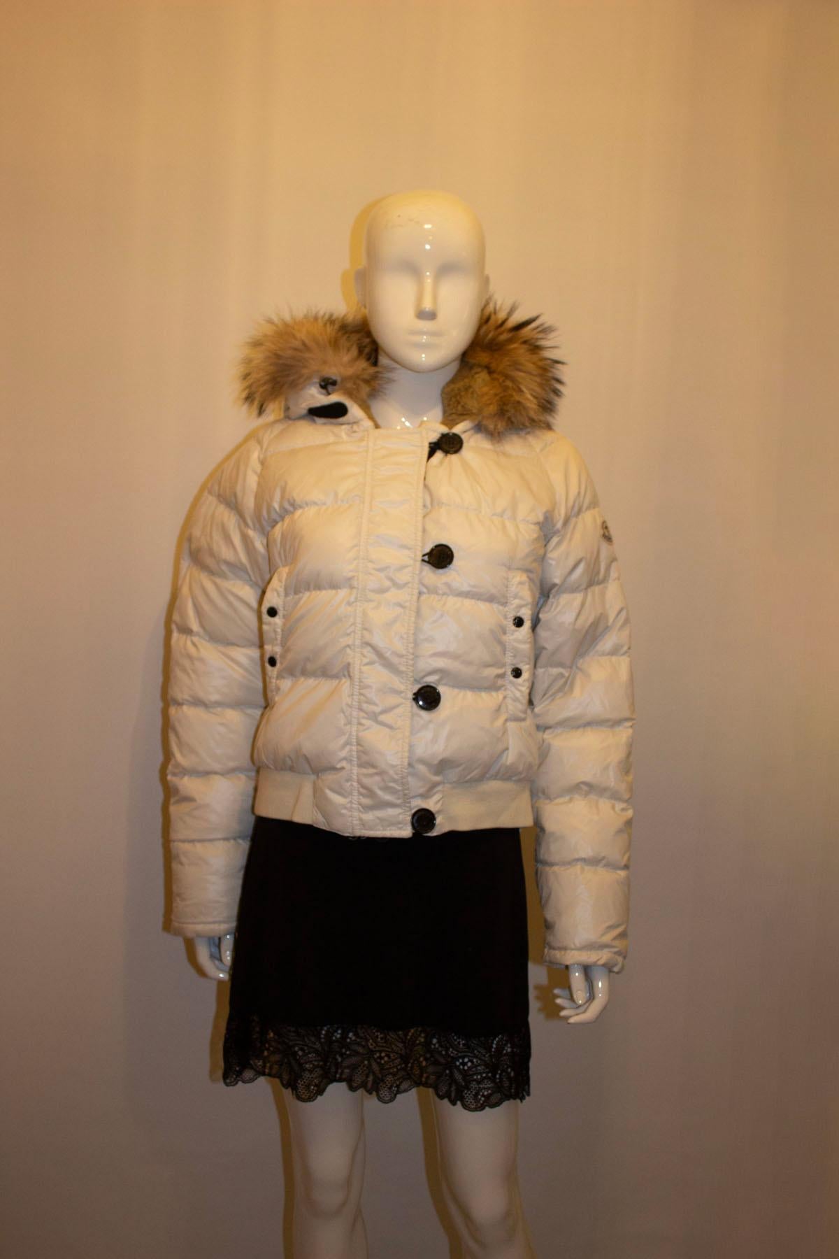 A great jacket for Fall/ Winter by Moncler. The jacket is in a white colour, with zip front fastening and four buttons - stamped Moncler. It has a  popper pocket on either side. The jacket has a elastic base and cuffs. it has an attached hood with