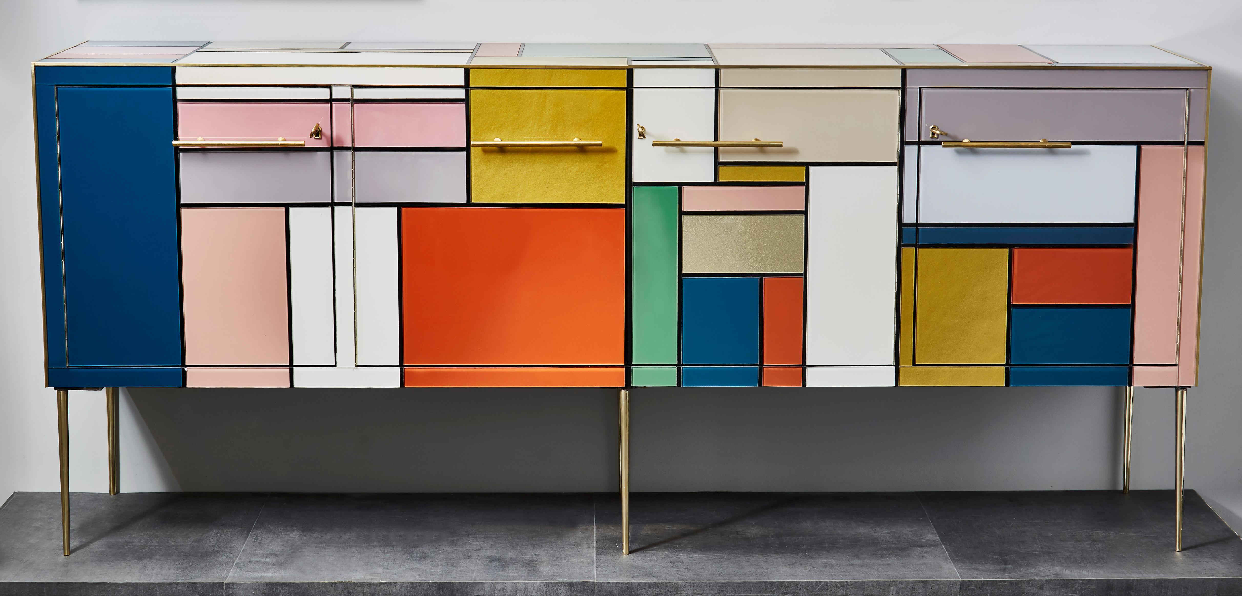 This vintage sideboard's has been customized by the Studio Glustin, and gets inspired by Piet Mondrian's abstract paintings. Composed with geometrical colored mirrors circled with brass inlays, it has four doors and remains on six brass feet.