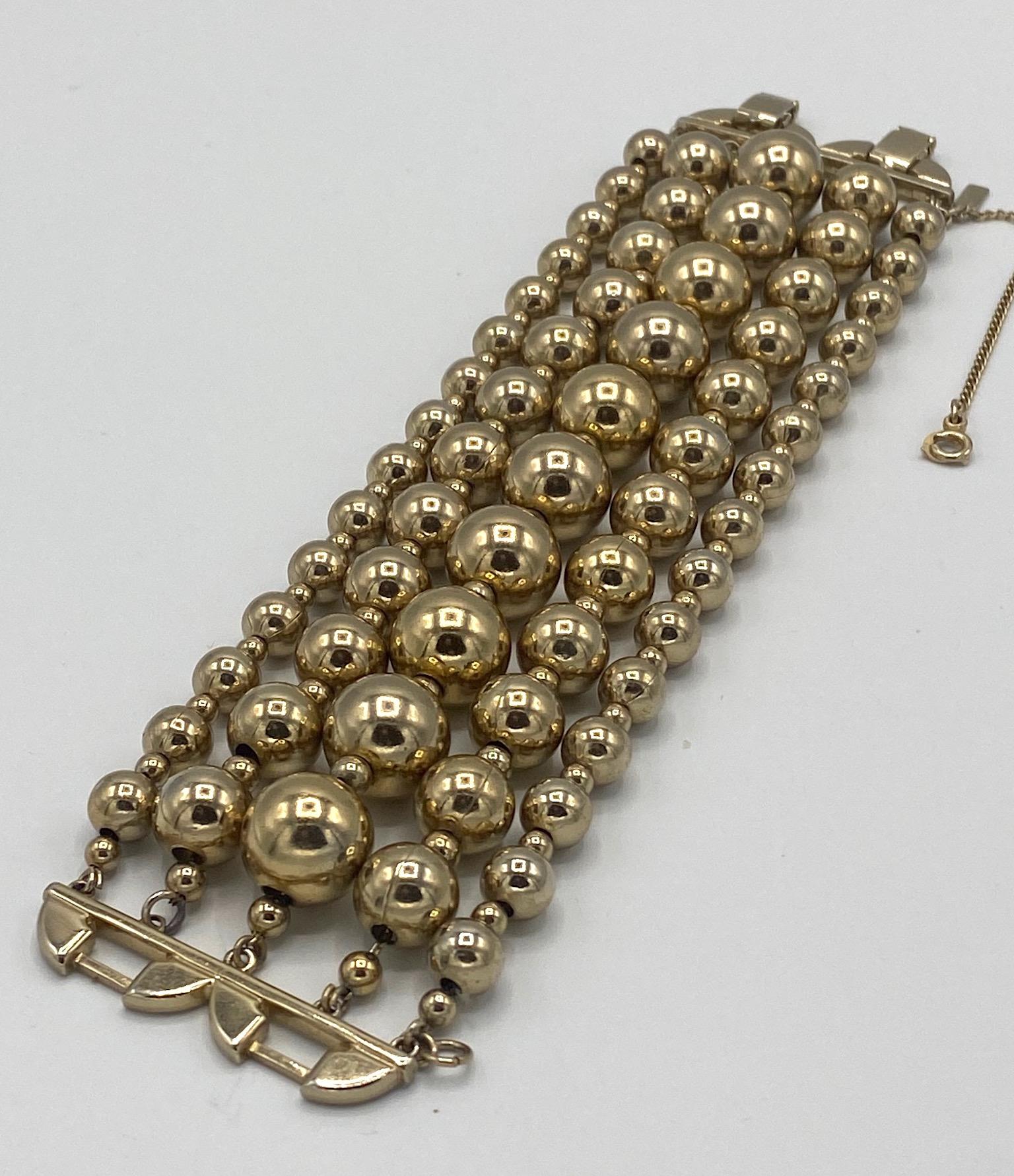 An elegant and wide gold bead bracelet by famous US company Monet circa 1950. Each strand consists of larger beads interspersed with .13 of a inch diameter small spacer beads and strung on chain. The central strand has large .5 inch diameter beads