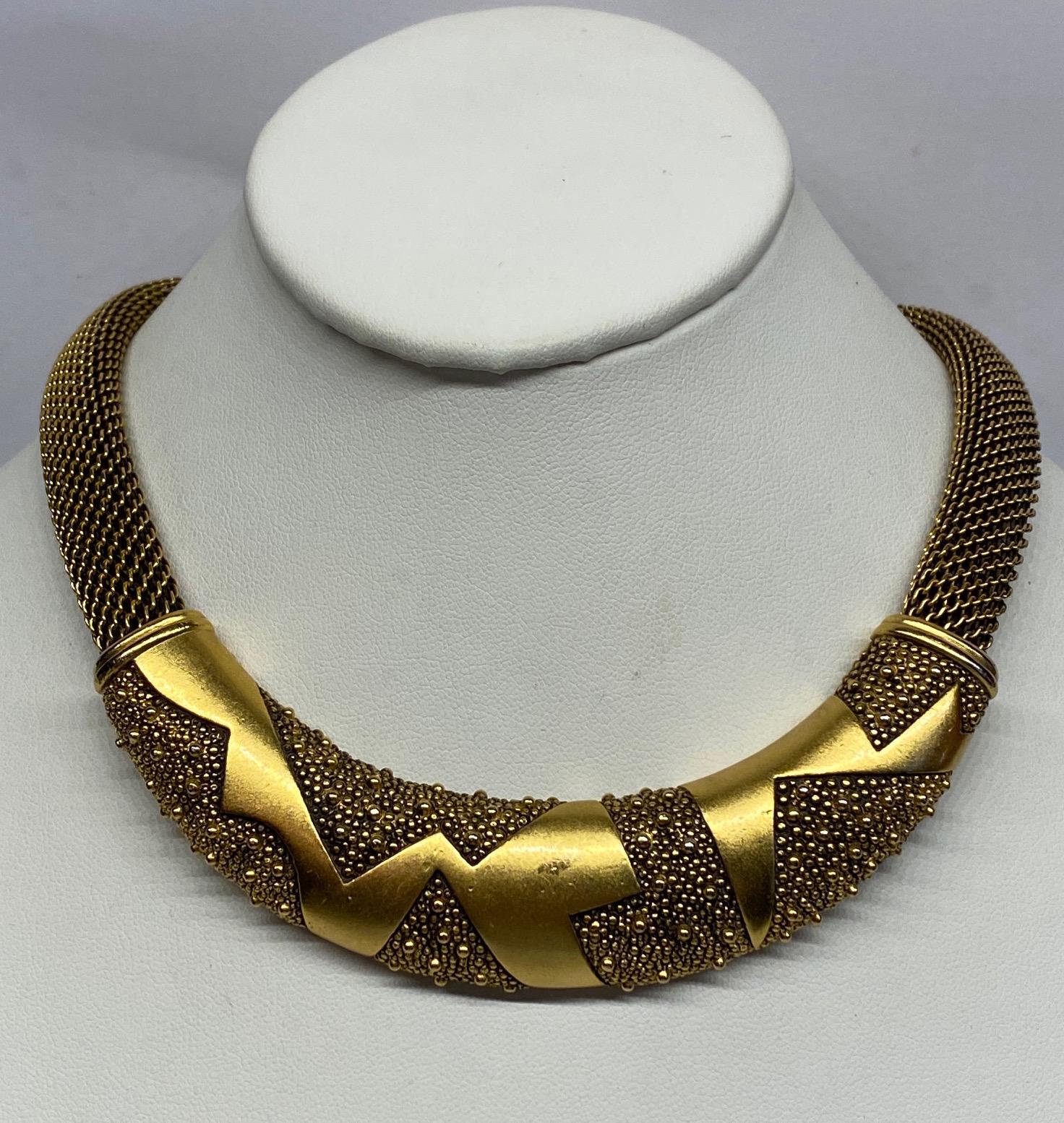 A wonderful abstract design and antique satin gold finish necklace by Monet from the 1980s. The necklace side strand are a half inch woven mesh link. The solid center piece is 4.5 inches widened .88 of an inch high. The piece is smooth with a