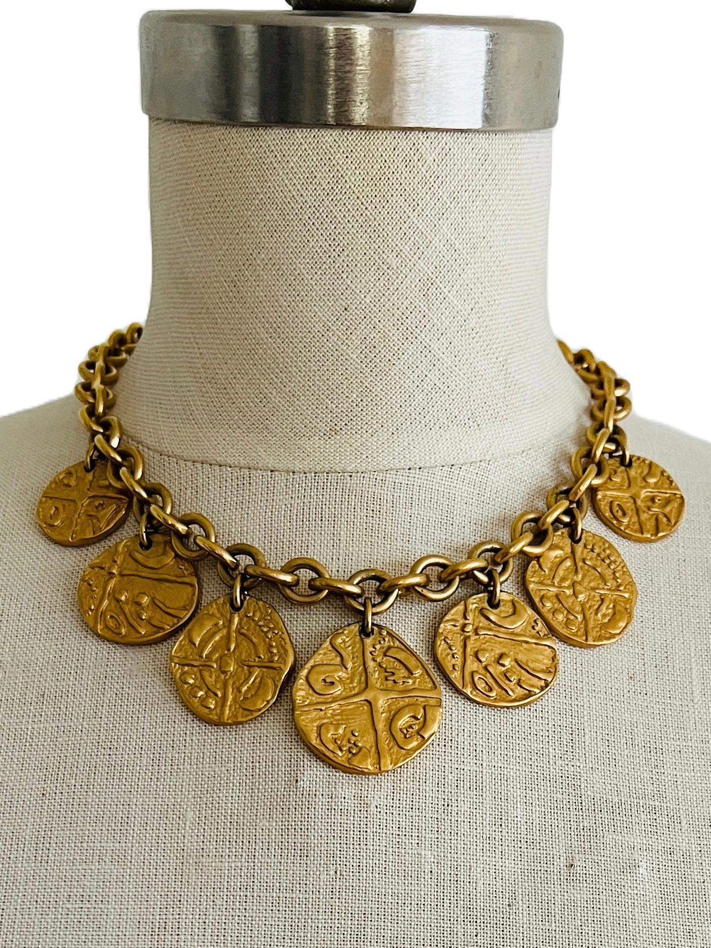 This striking vintage Monet coin necklace choker channels the grandeur of ancient civilizations with its bold and detailed design. Featuring seven substantial medallion-style coins suspended from a chunky gold-tone chain, each coin is embossed with