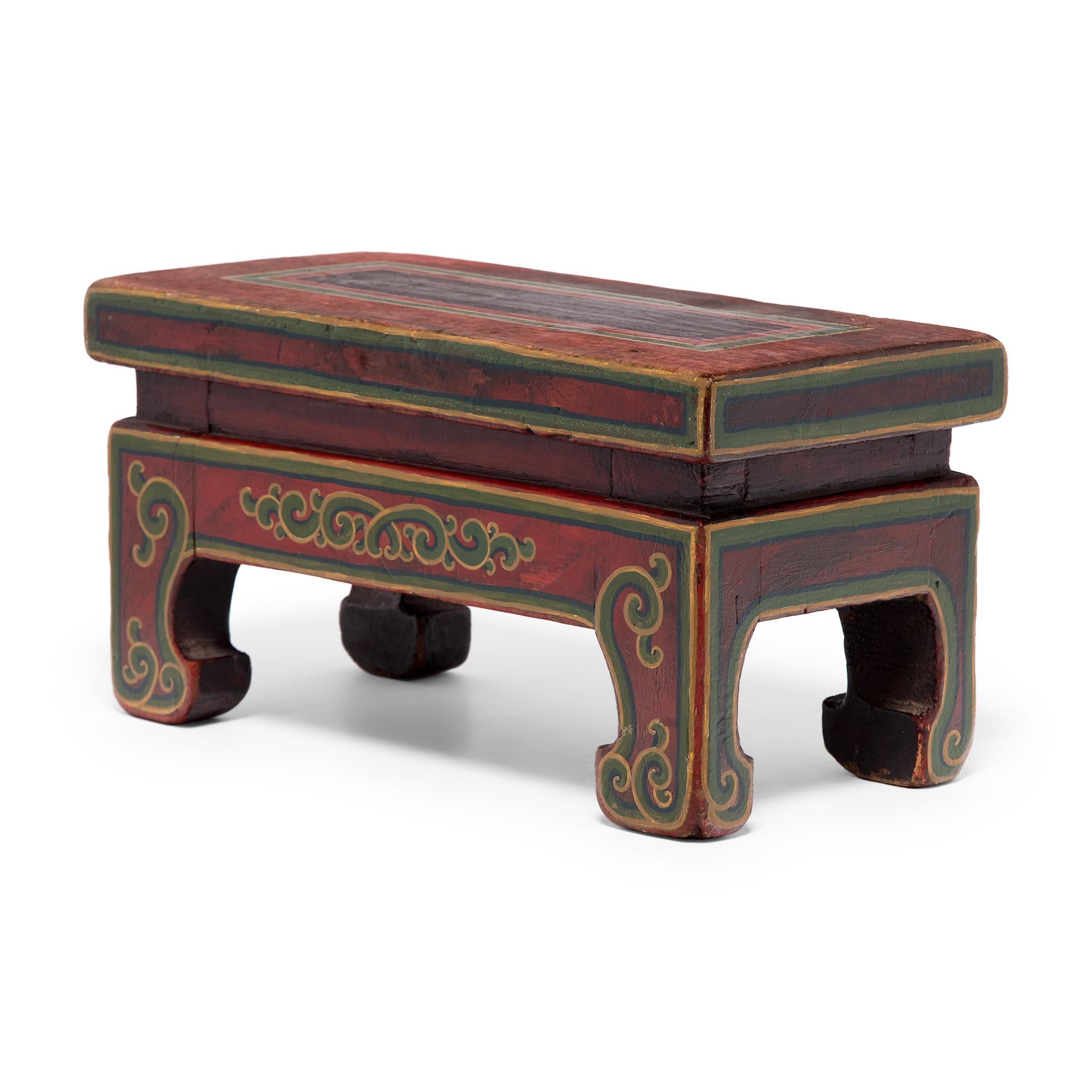 Resembling a low kang table, this small table stand is simply shaped with a waisted apron and four short legs ending in hoof feet. Decorated in the style of Mongolian and Tibetan furniture, the stand is painted red on all sides and outlined by a