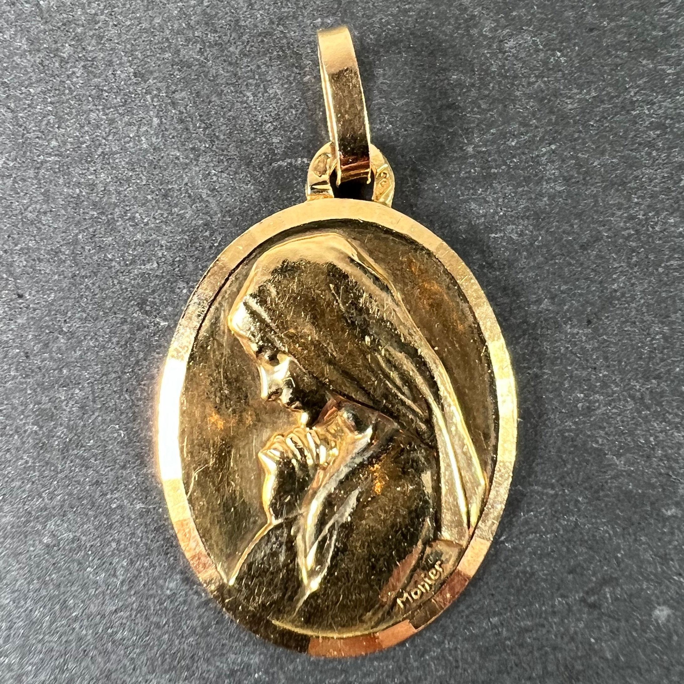 A French 18 karat (18K) yellow gold charm pendant or medal designed by Monier depicting the profile of the Virgin Mary at prayer, surrounded by a faceted frame. Stamped with the eagle's head for French manufacture, the makers mark for Perriat, and