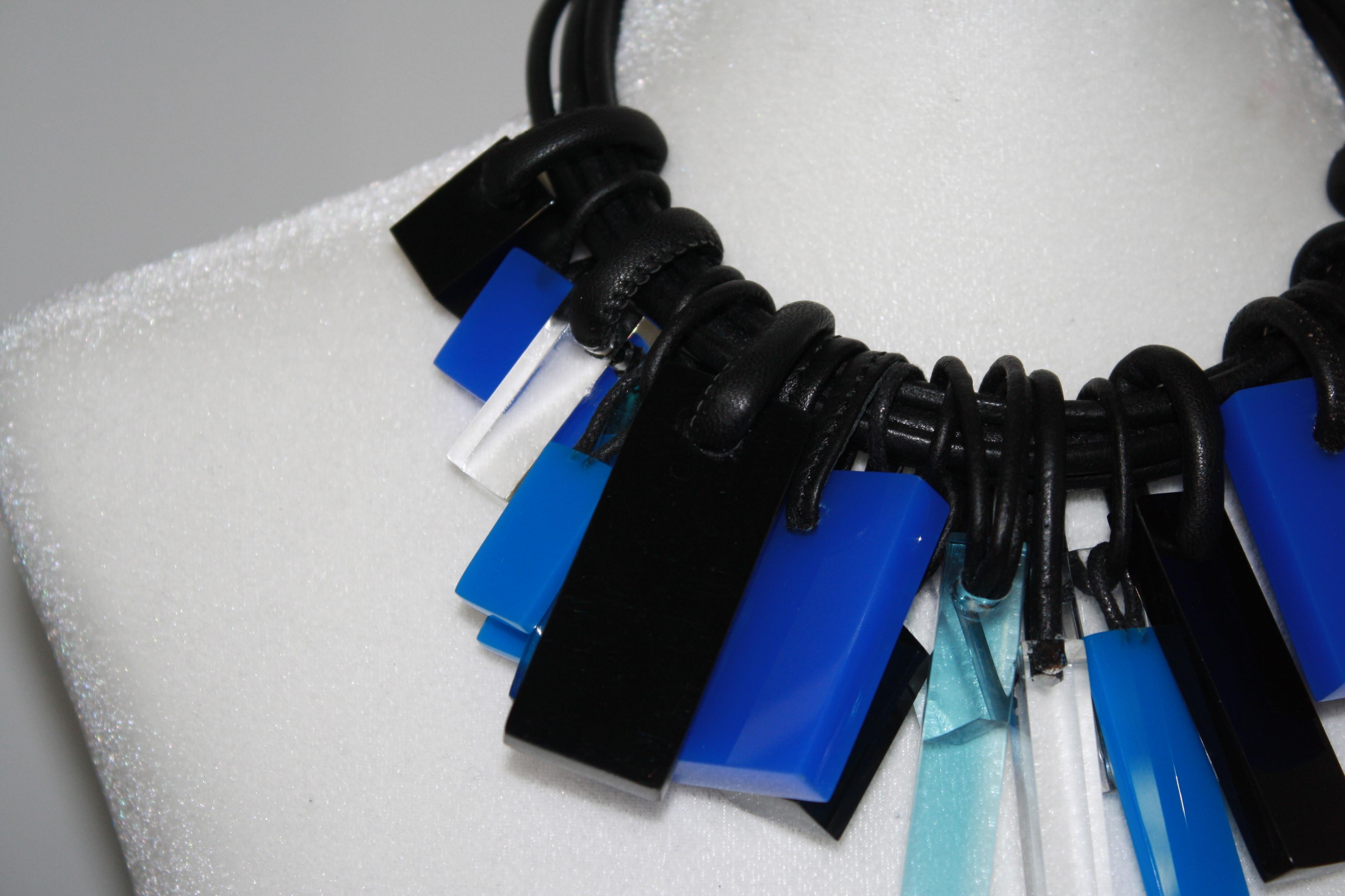 5 strands of black leather with a hook and eye clasp finished with a cube of acrylic. Black, blue polyester i and clear acrylic geometric shapes with leather rings are sliding on the choker..
A fabulous statement necklace you can wear all year round.