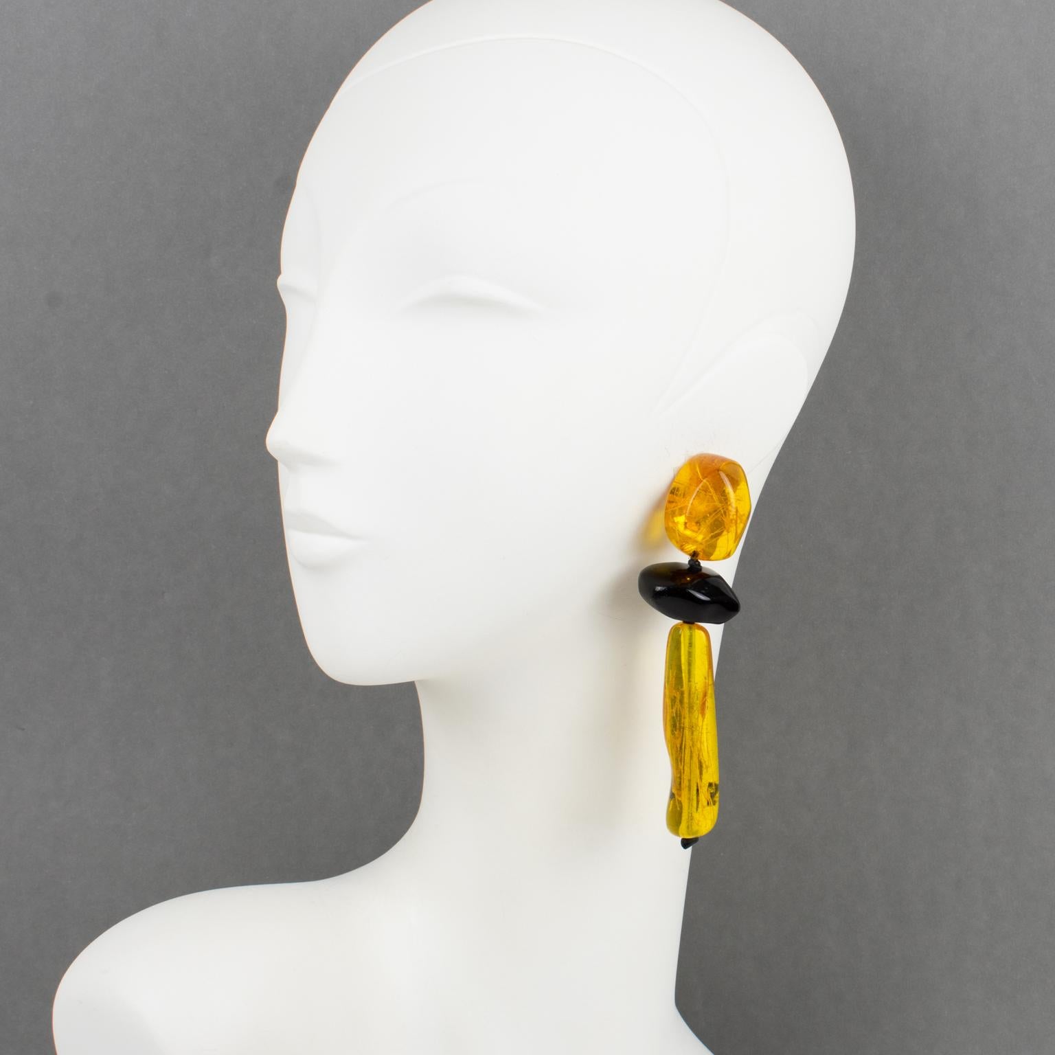 Gerda Lyngaard for Monies designed these stunning oversized dangle clip-on earrings. The pebbles-shaped design is all hand-made and hand-carved using resin with inclusions. The shiny black elements are contrasted with burnt orange amber long drops