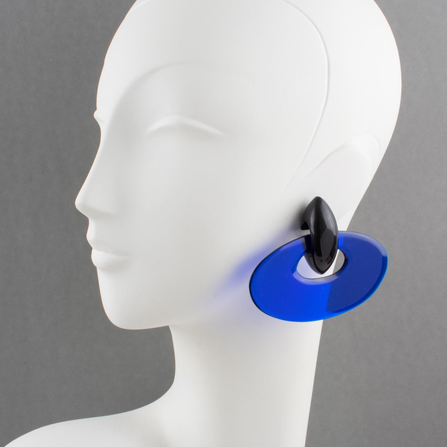 Charming oversized clip-on earrings by Gerda Lyngaard for Monies. Dangling extra-large ellipse donut in transparent cobalt blue resin contrasted with Ebony wood drop element. Marked 