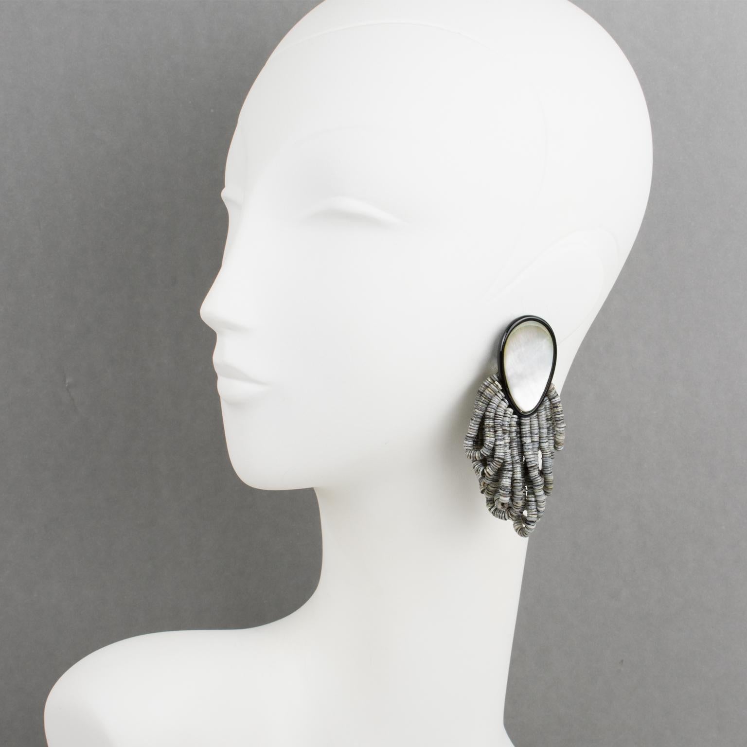 Elegant oversized dangling clip-on earrings designed by Gerda Lyngaard for Monies. These earrings feature smooth hand-carved teardrop black resin shapes ornate with seashell elements. They are ornate with tiny gray and white seashell seed beads in a