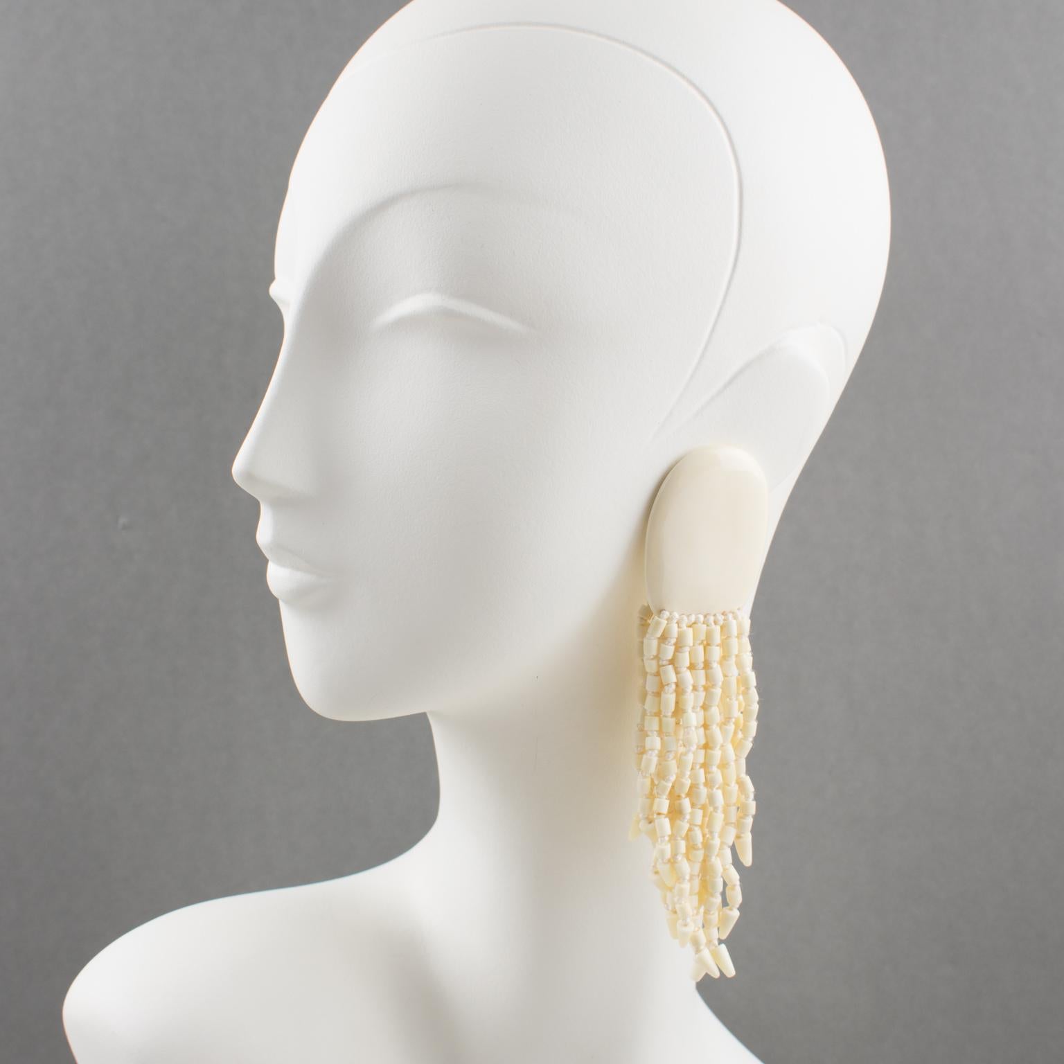 Stunning oversized clip-on earrings by Gerda Lyngaard for Monies. Dimensional large pebble ornate with multi-strand dangling charms in bovine bone elements. Lovely silky off-white color. Marked 'Monies' on each ear clip. 
Measurements: 5.50 in. long