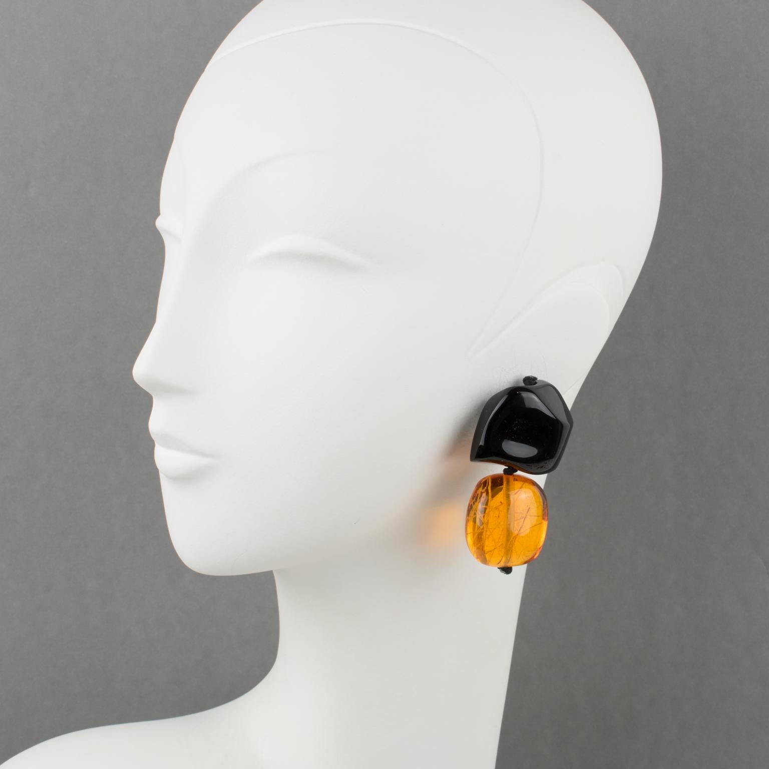 Stunning oversized clip-on earrings by Gerda Lyngaard for Monies. Hand-made dangling pebbles carved shape in Lucite or resin with inclusions. Assorted color of shiny black and burnt orange-amber with threads inclusions. Marked 