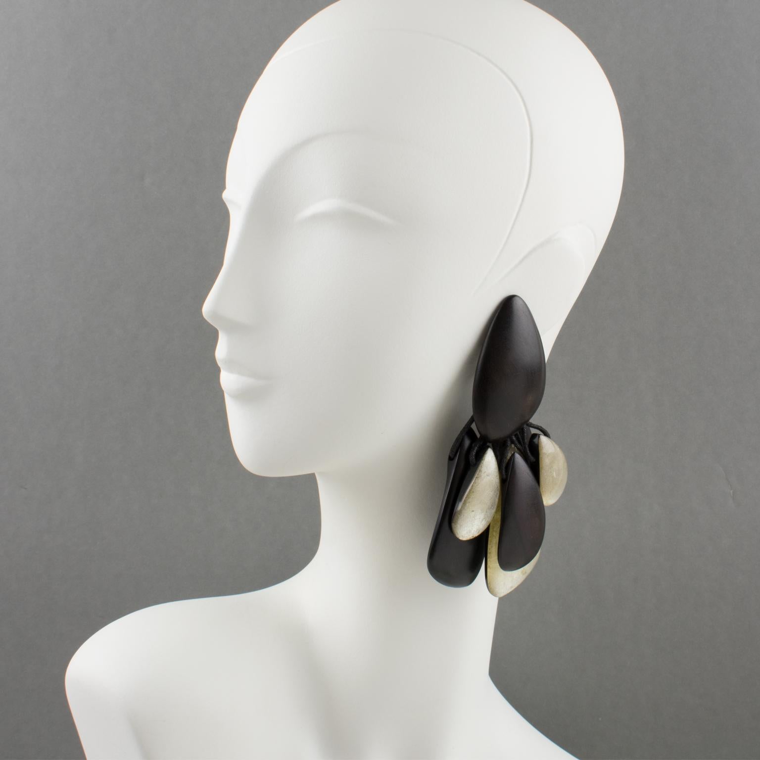 Gerda Lyngaard for Monies designed those stunning oversized hand-made clip-on earrings. The dangling pebble shape boasts charms in natural Ebony wood and resin. The resin pebbles are black on the background and pearlized on the front with silver