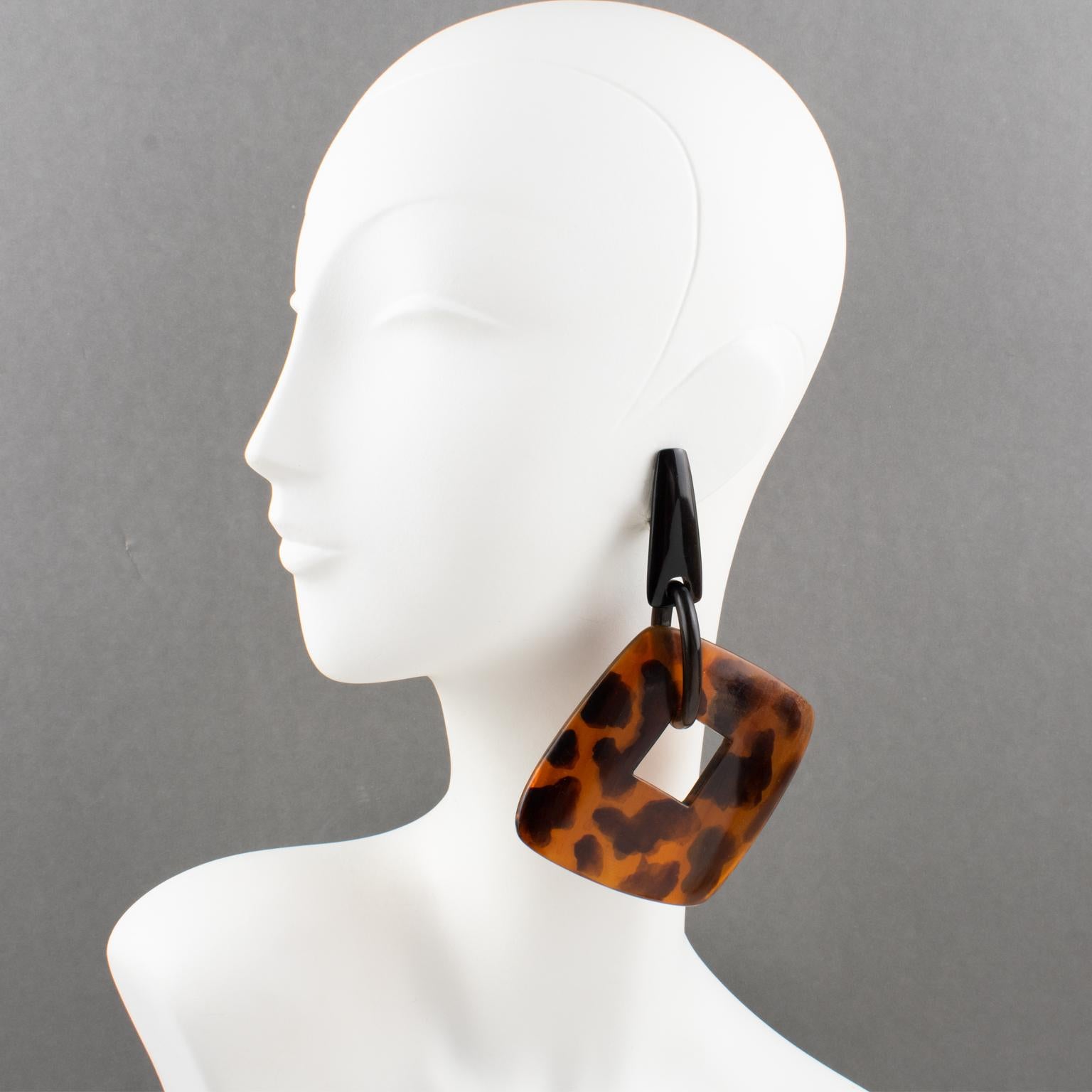 These beautiful oversized clip-on earrings by Gerda Lyngaard for Monies feature a dangling geometric shape with a massive square donut in tortoise (tortoiseshell) resin in a very organic flair. The geometric fastenings in resin are carved and