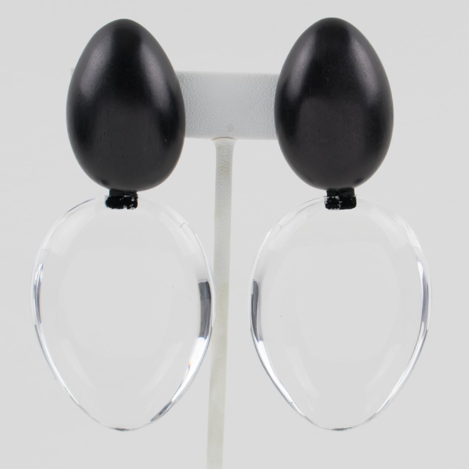 These incredible oversized clip-on earrings designed by Gerda Lyngaard for Monies feature a dangling pebble teardrop shape in transparent Lucite with Ebony wood egg-shaped clip fittings. The earrings are marked 