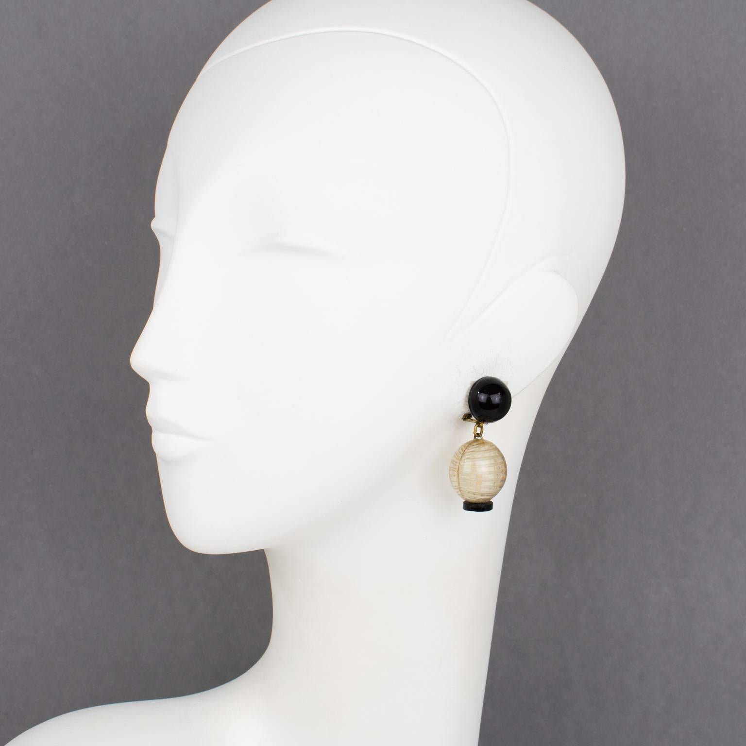 Ces fabuleuses boucles d'oreilles Monique Vedie en résine ou Talosel à clipser présentent une forme pendante inspirée d'un motif de lanterne traditionnelle japonaise ou asiatique. Le modèle présente des boutons de fermeture noirs et des éléments
