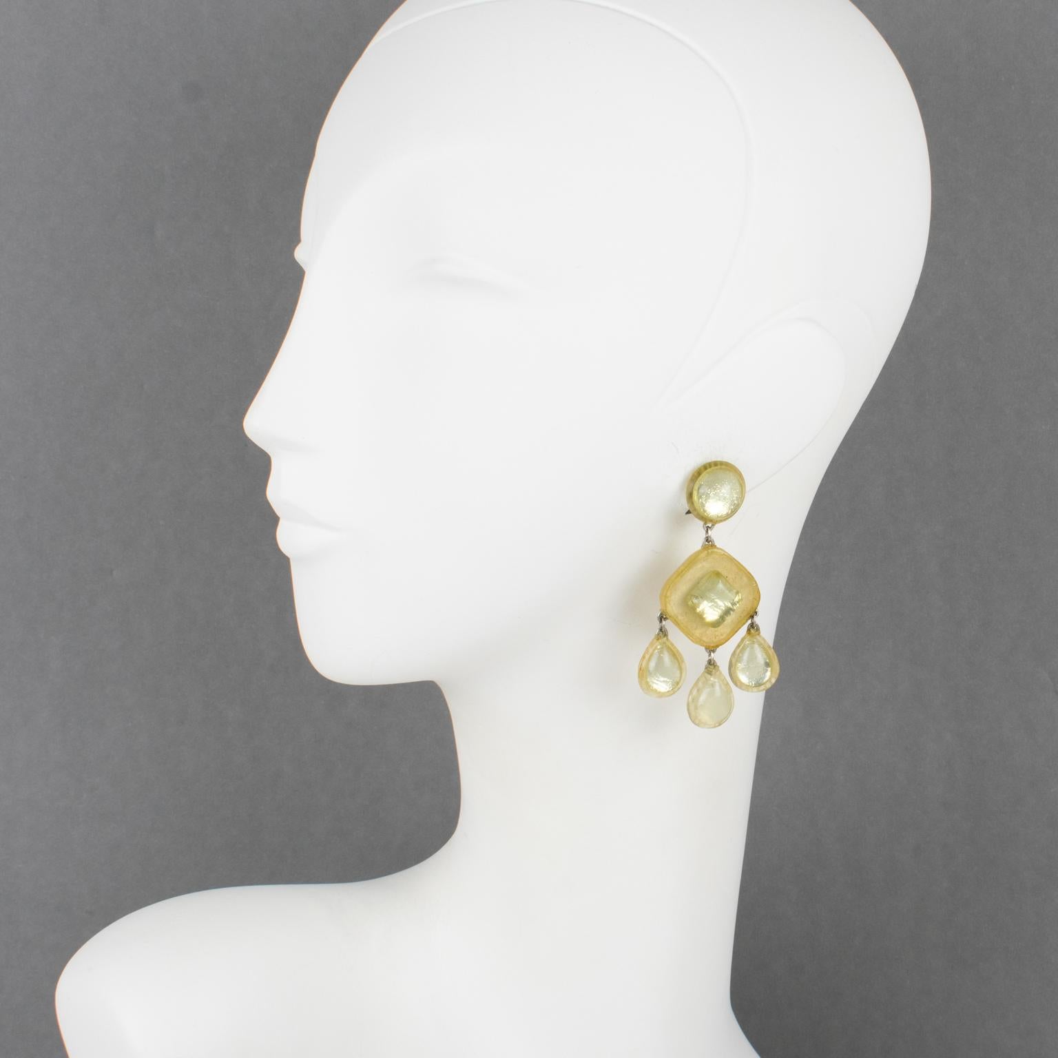 Refined Monique Vedie Talosel or resin clip-on earrings. They feature a geometric dangling shape with frosted and mirrored textured patterns in pale yellow color. The fastening clips at the back are marked 