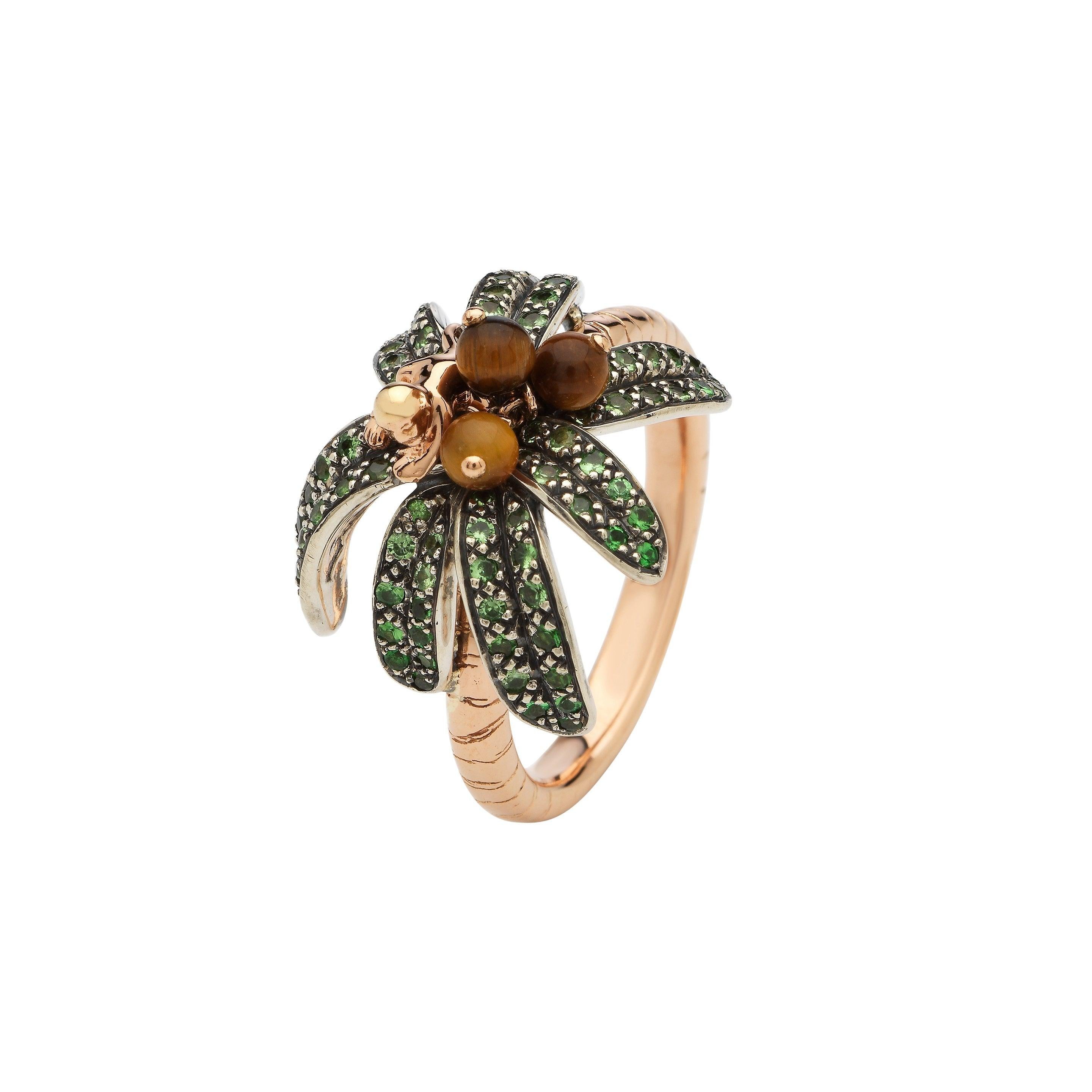 A baby monkey crafted from 18k rose gold clambers amid palm leaves embellished with green tsavorites on this 18k rose gold ring. With its band textured to evoke a palm tree’s trunk, tiger’s eye coconuts are also set on the ring, that gently move as