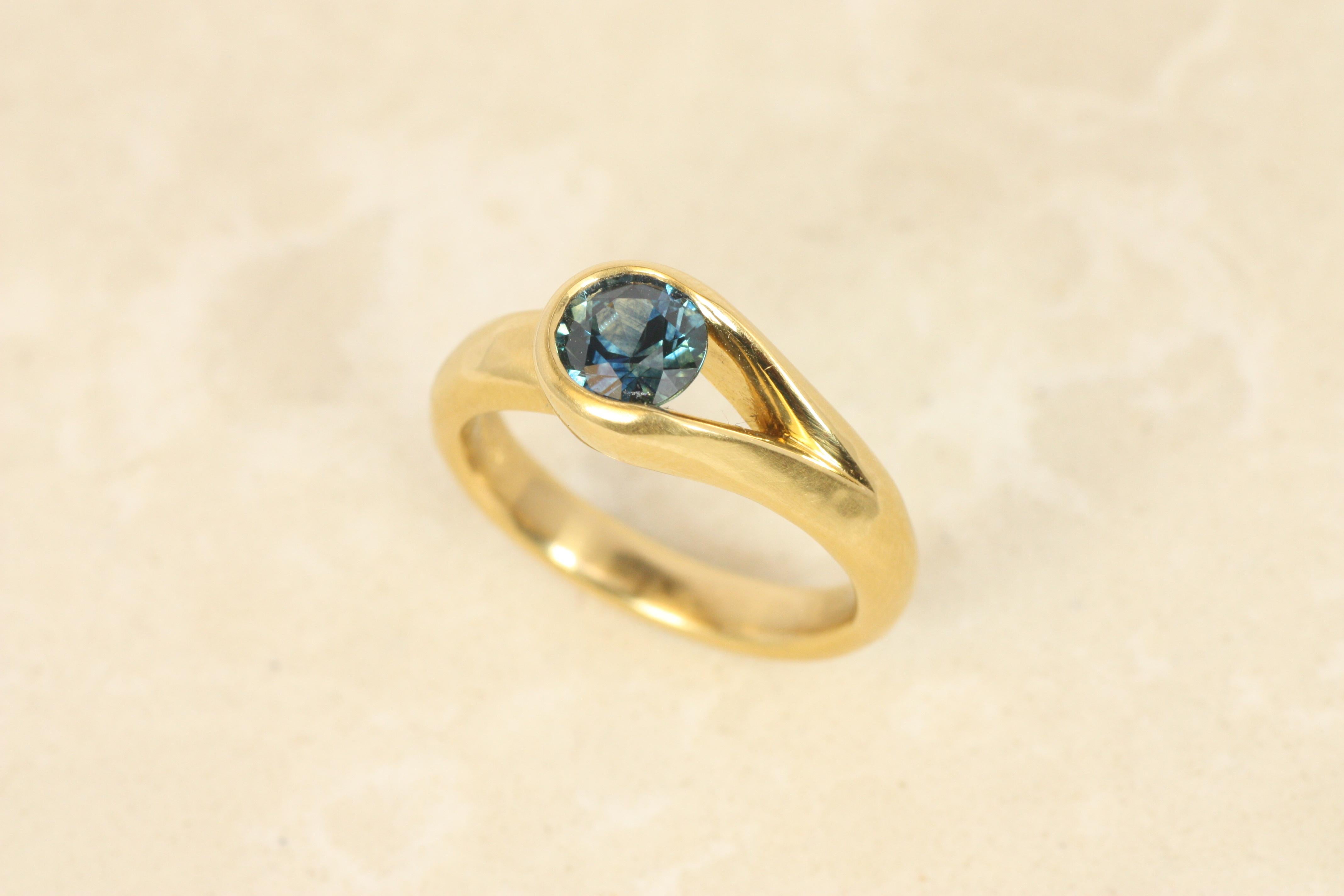 Dieser asymmetrische Ring ist eine Neuinterpretation eines klassischen Solitärs. Die seitlich offene Lünette hebt den blauen Montana-Saphir von 0,97 Karat hervor, so dass das Licht seine Brillanz voll zur Geltung bringt. Dieser Ring aus