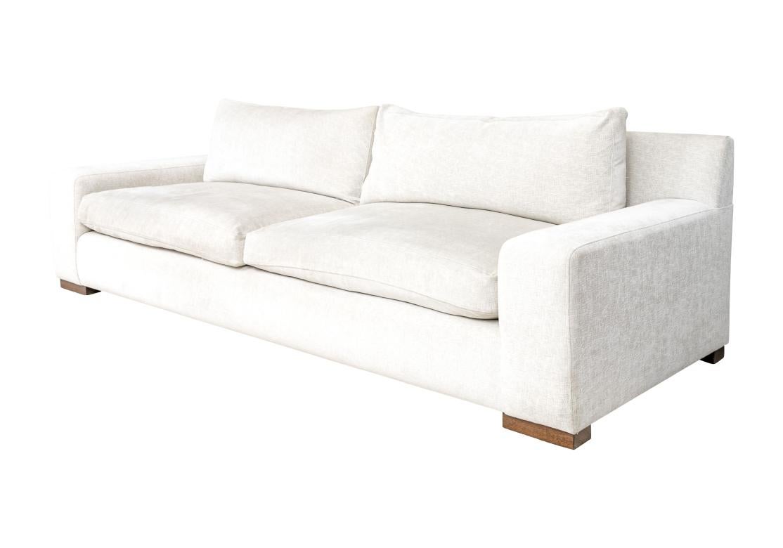 Eines der klassischen Montauk-Sofas mit hohen flachen Arm- und Rückenlehnen. Zusammen mit einem Paar Rücken- und Sitzkissen, gepolstert mit einem feinen, neutralweißen Stoff. Auf flachen braunen Holzfüßen stehend. Hergestellt in