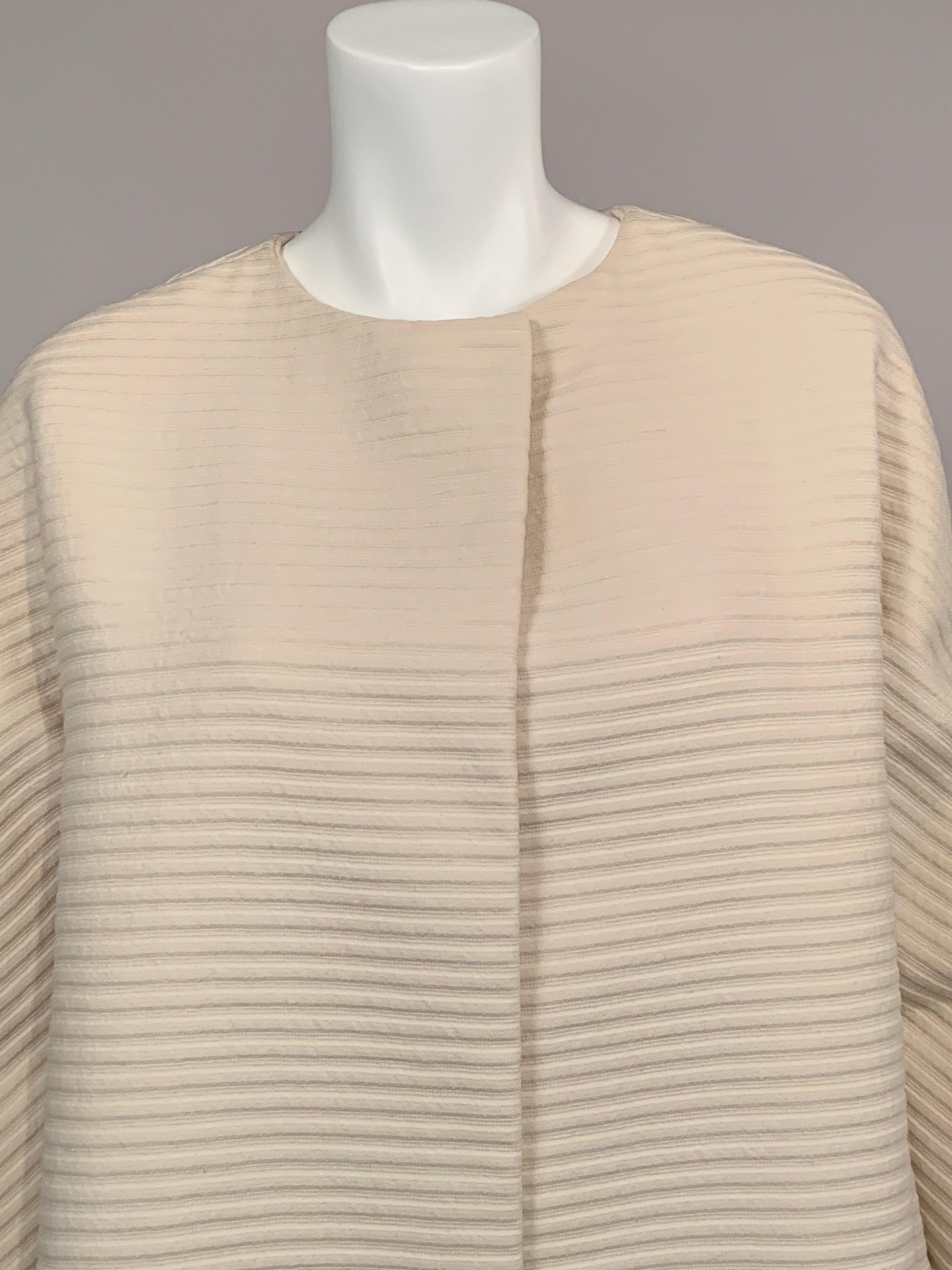 Dieser cremefarbene Mantel aus gerippter Wolle wurde in New York City von Monte-Sano & Pruzan entworfen, einem angesehenen Modehaus, das für seine Schneiderkunst bekannt ist. Er ist klassisch elegant.  Der Mantel ist kragenlos, mit doppelten