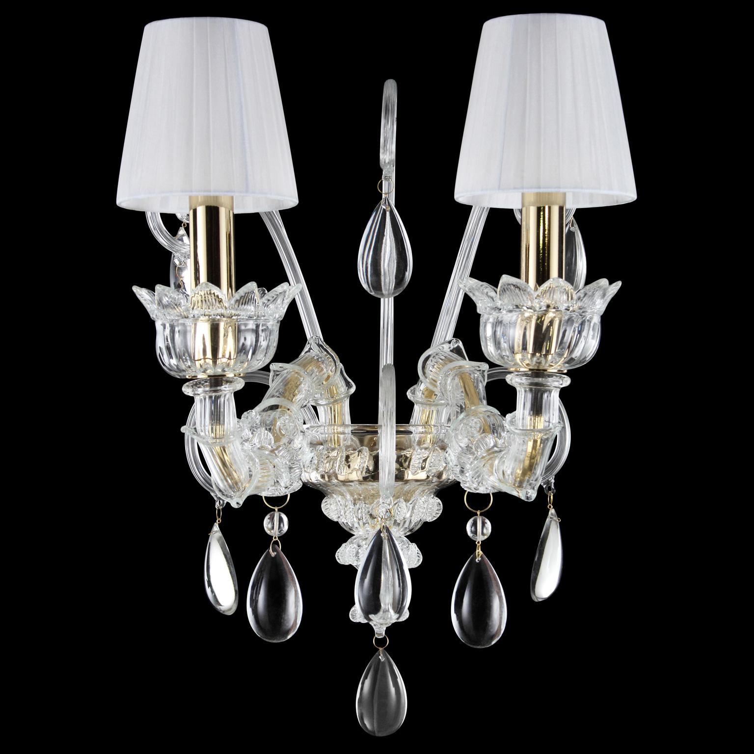 Montecristo de pared, 2 luces, cristal artístico, pantallas de organza blanca de Multiforme.
La colección Montecristo está creada con los elementos típicos de las lámparas de cristal venecianas. De la columna central, decorada con 