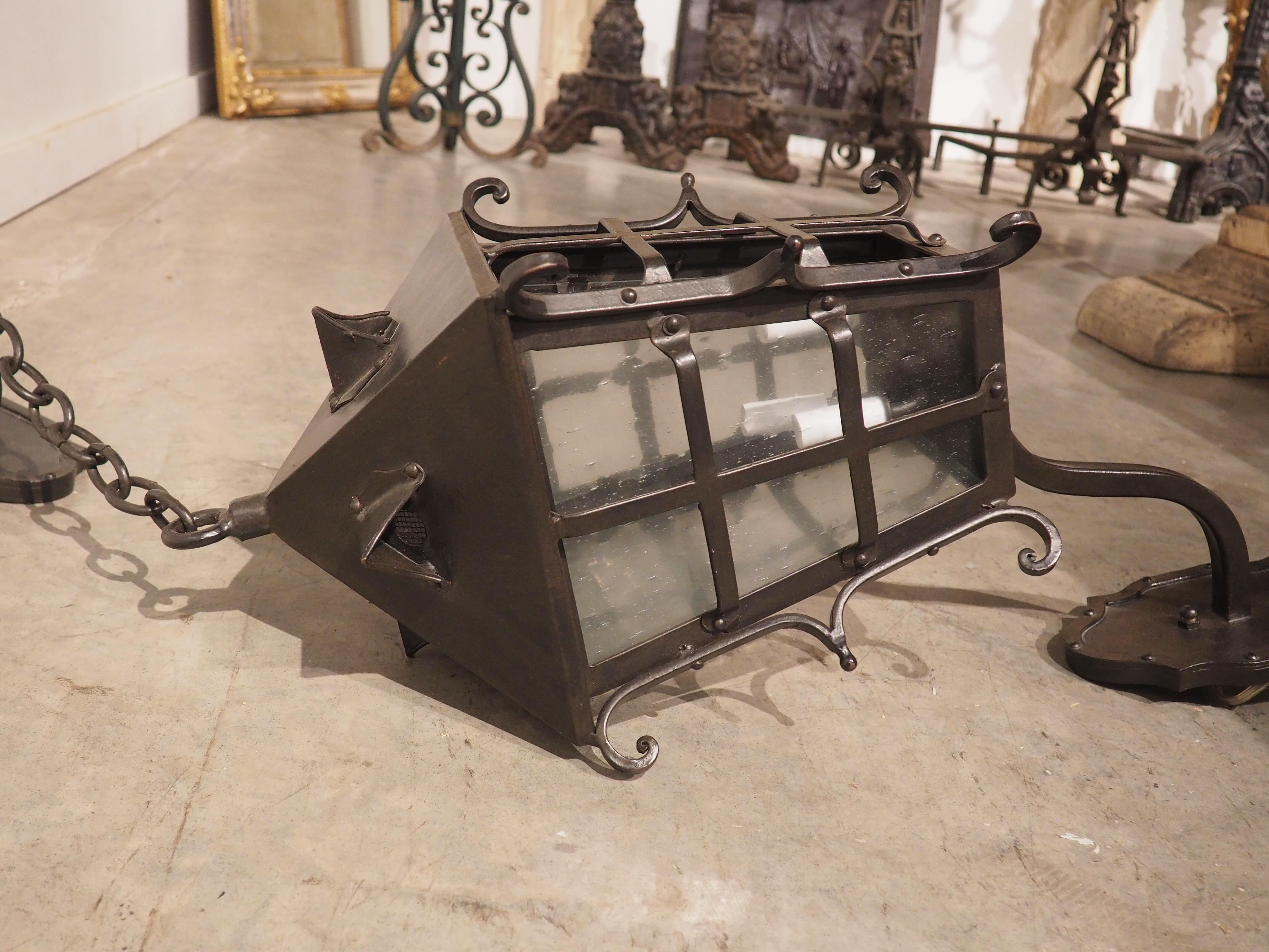 Spanish blacksmiths of the Renaissance period were known for their elaborate pieces that typically featured scrolled elements and imaginative crests. This wrought iron lantern with chained wall mount is reminiscent of such antique Spanish work. The