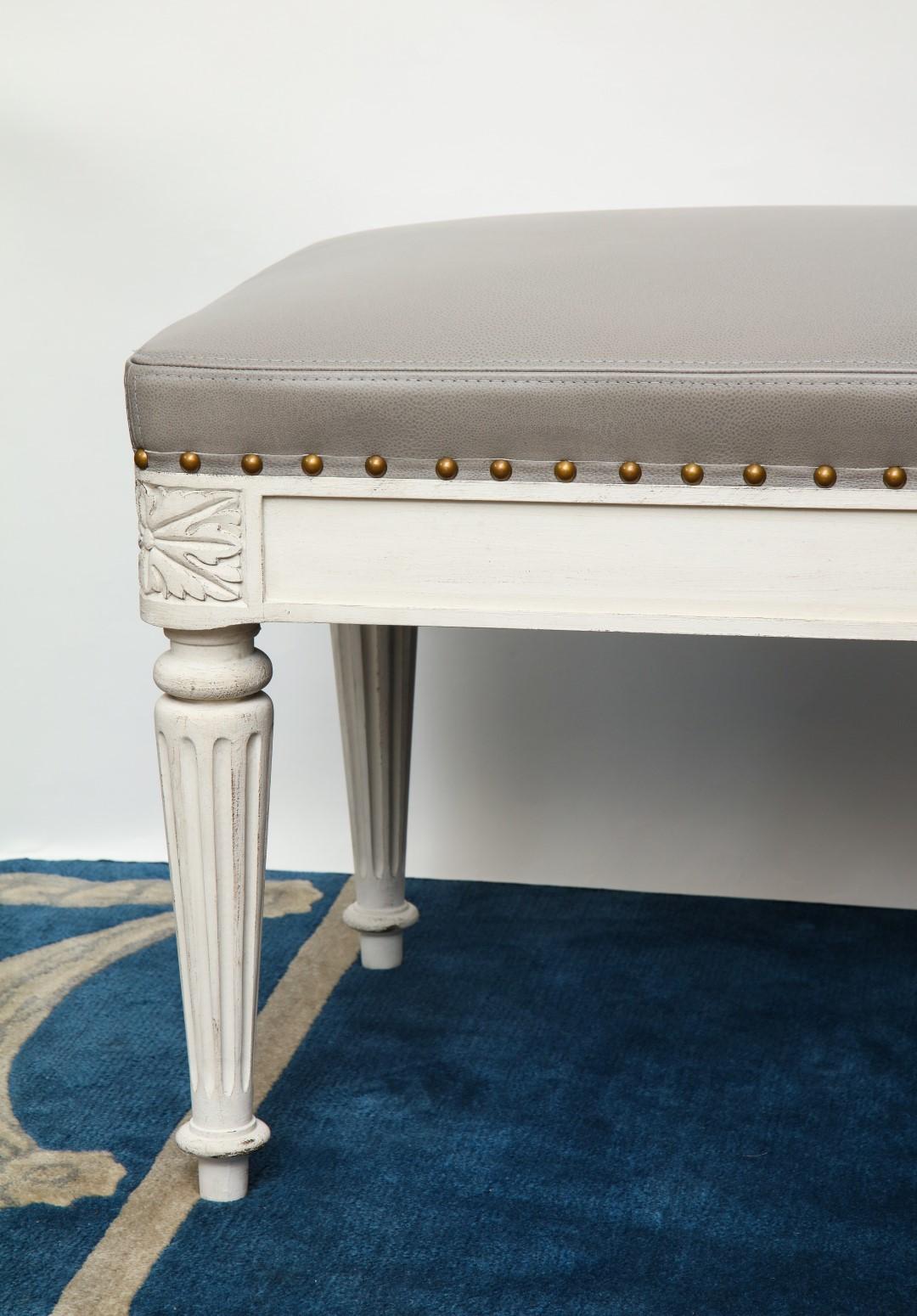 The Montreuil Bench, a custom bench designed by David Duncan. This Louis XVI-style, rectangular bench features a leather upholstered seat trimmed with nail heads above apron. With rounded corners that showcase hand carved rosettes, the bench also