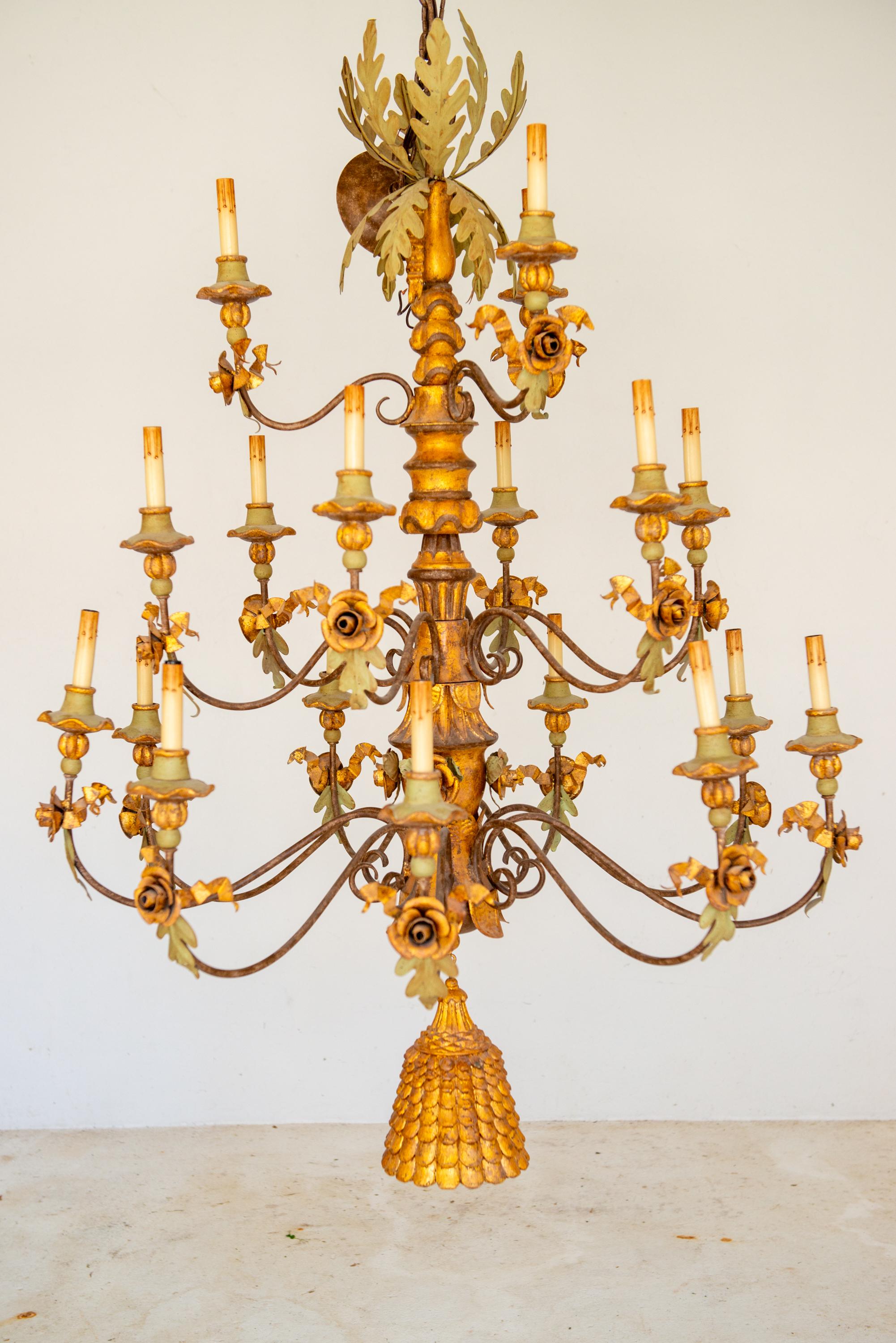Large three tiered gesso, gilt wood, wrought iron 18 light Italian chandelier.
Embellished with an oversized pinecone style finial, tole leaves, tole ribbons, tole roses, gilt and painted gesso bobeches. Includes original canopy. A stunning