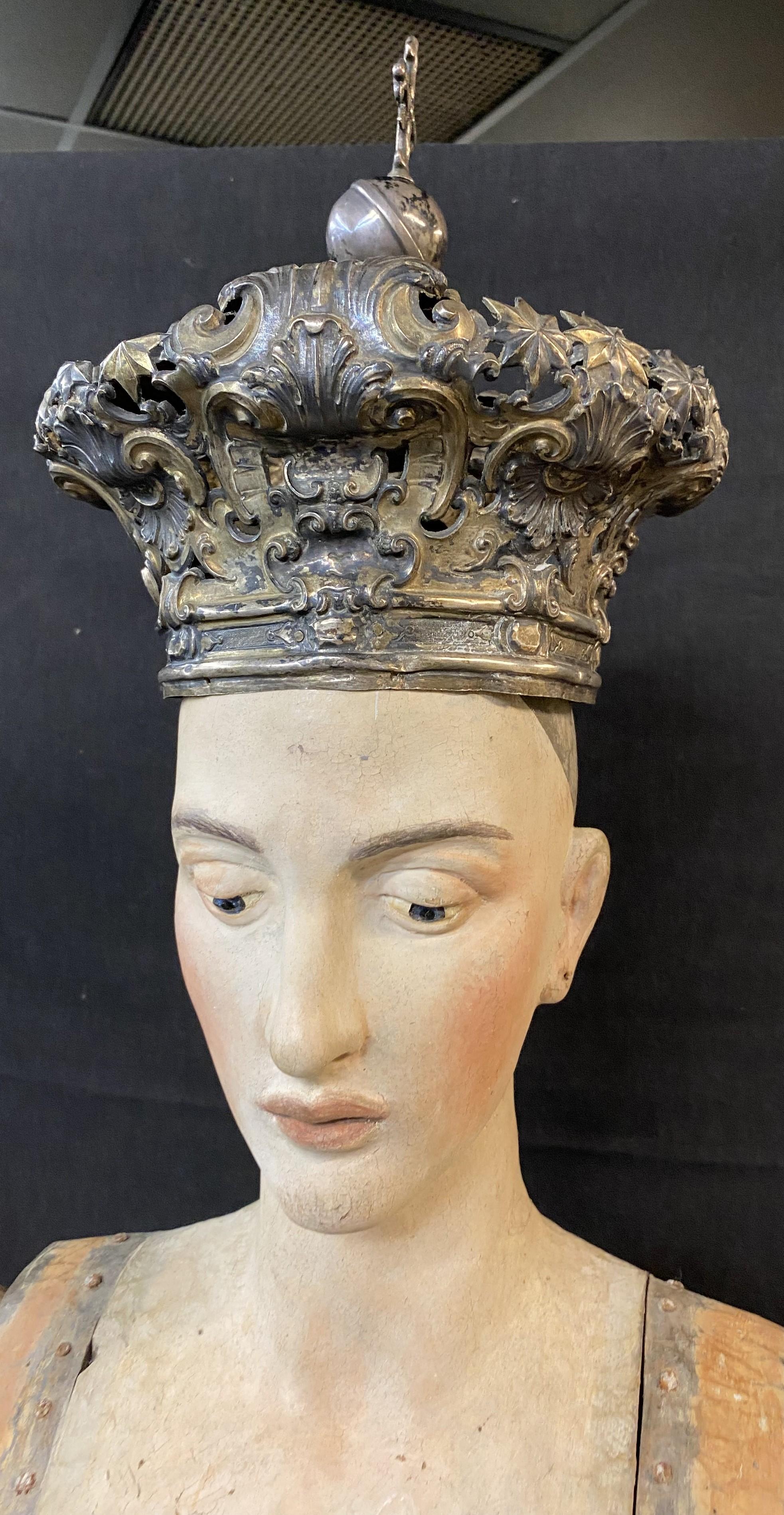 An impressive large carved polychrome cage doll santos with fine facial details, detachable hands, jointed arms with attaching hooks, on an oval wooden base, and includes an unmarked antique metal crown. The santos is probably Italian in origin,