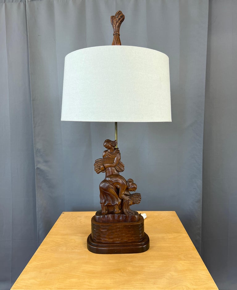 Offered here is a monumental 1940's carved Mahogany table lamp, it's design is of women harvesting wheat.
Carved into it's back side is the maker's name Heifetz.

Measurements below are of it's base and to the top of it's finial. 
Carving of the