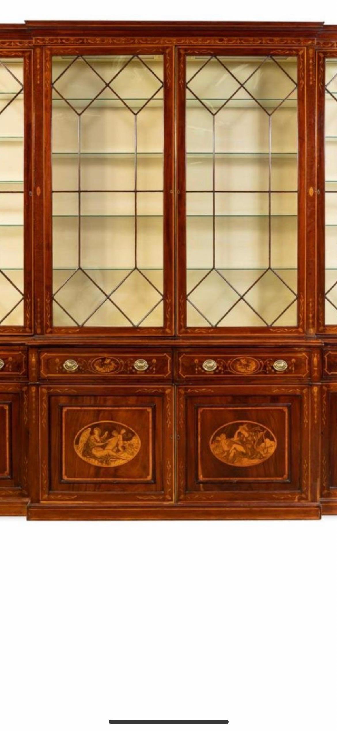English, early 19th century, monumental mahogany and mahogany veneered marquetry inlaid Georgian breakfront cabinet having a shaped cornice above four astragal glazed doors, with four doors below having mythological scenes and musical trophies, on a
