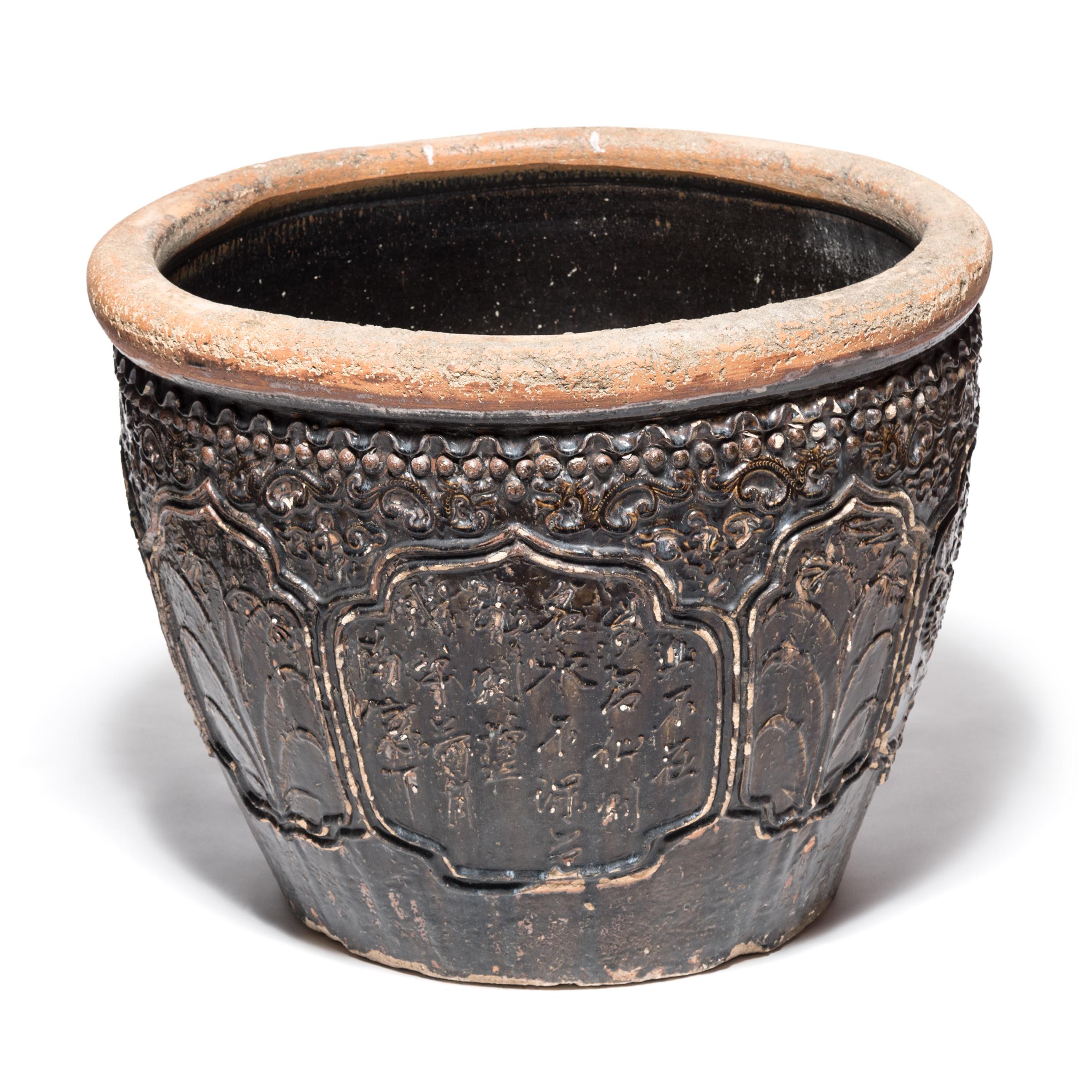 This late 19th century monumental glazed ceramic urn from southern China was originally used for pickling food. Its sculpted high-relief surface depicts floral medallions and abstract dragons, symbols of power and good fortune.