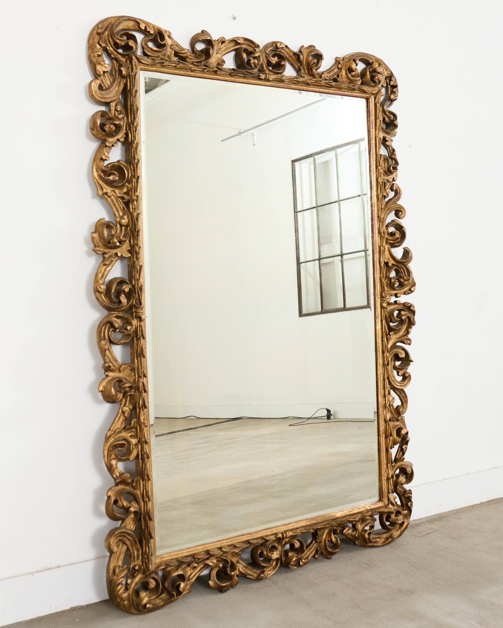Imposing 19th century Italian carved floor mirror made on a grand monumental scale measuring over 6 feet tall. The mirror features a hand-beveled period thick glass plate mounted in a deep relief-carved gilt wood frame. The frame has elegant scroll