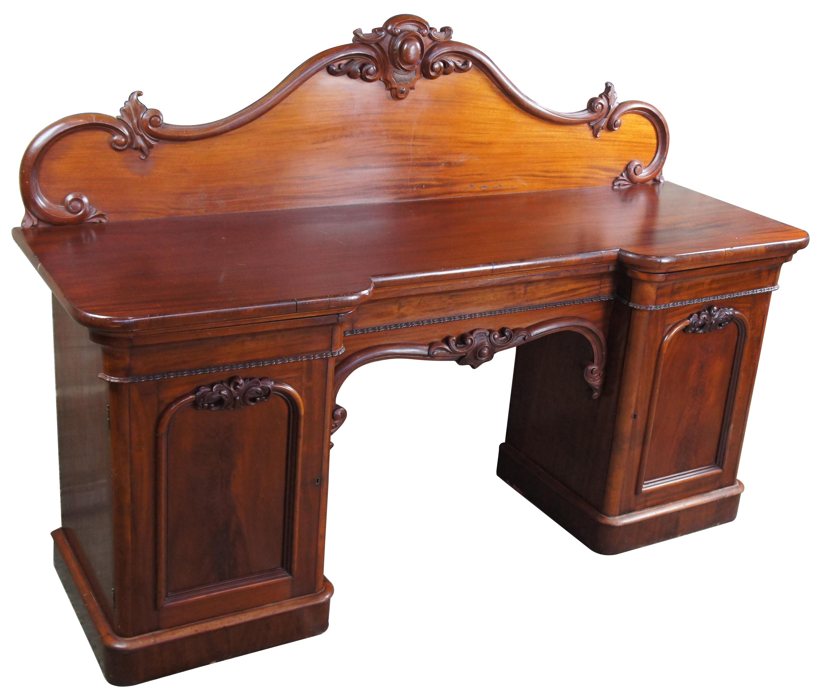 Solid mahogany monumental English sideboard or breakfront with flame mahogany veneers, circa 1820s. Features a large serpentine carved backsplash and a long central drawer flanked by outer cabinets. Could also be used as a console, buffet, credenza
