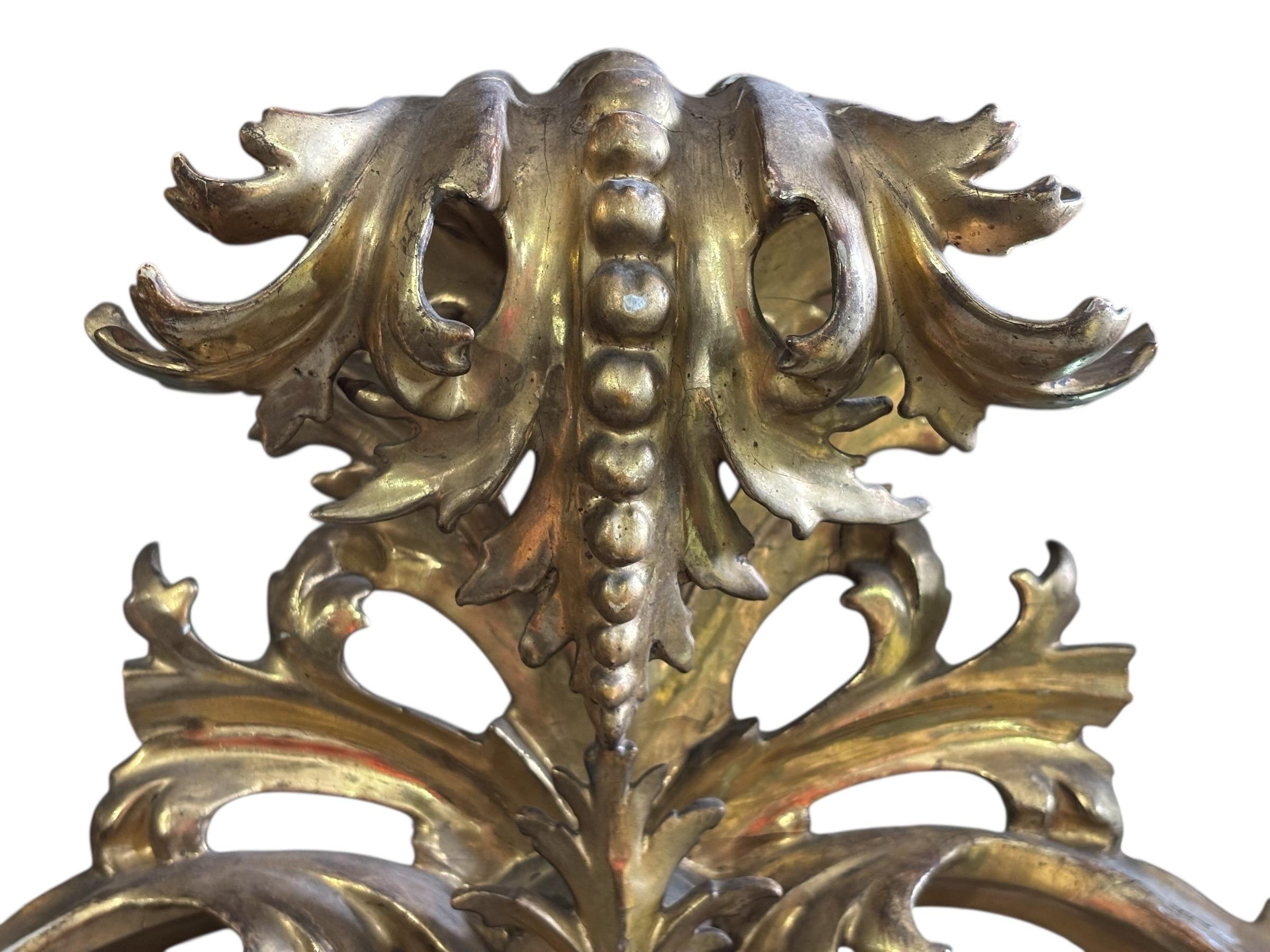 A monumental giltwood oval mirror made in Italy in the 19th century. The rococo frame is carved with a large pierced acanthus leaf crest that overhangs the frame with pierced lattice and scrolled acanthus all around. The center frame is beaded and