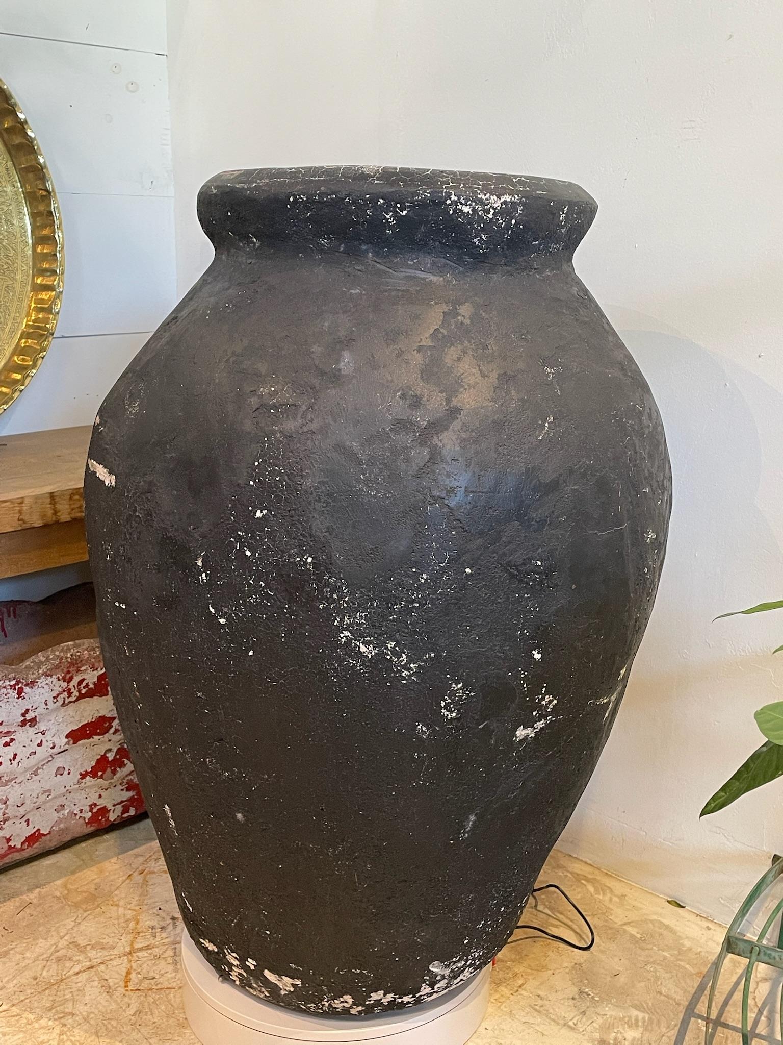 Questo monumentale vaso di terracotta nera è un pezzo imponente che unisce l'utilità antica all'arte scultorea. Realizzato a mano in modo tradizionale, il vaso presenta una forma audace e arrotondata che si restringe dolcemente verso la base,