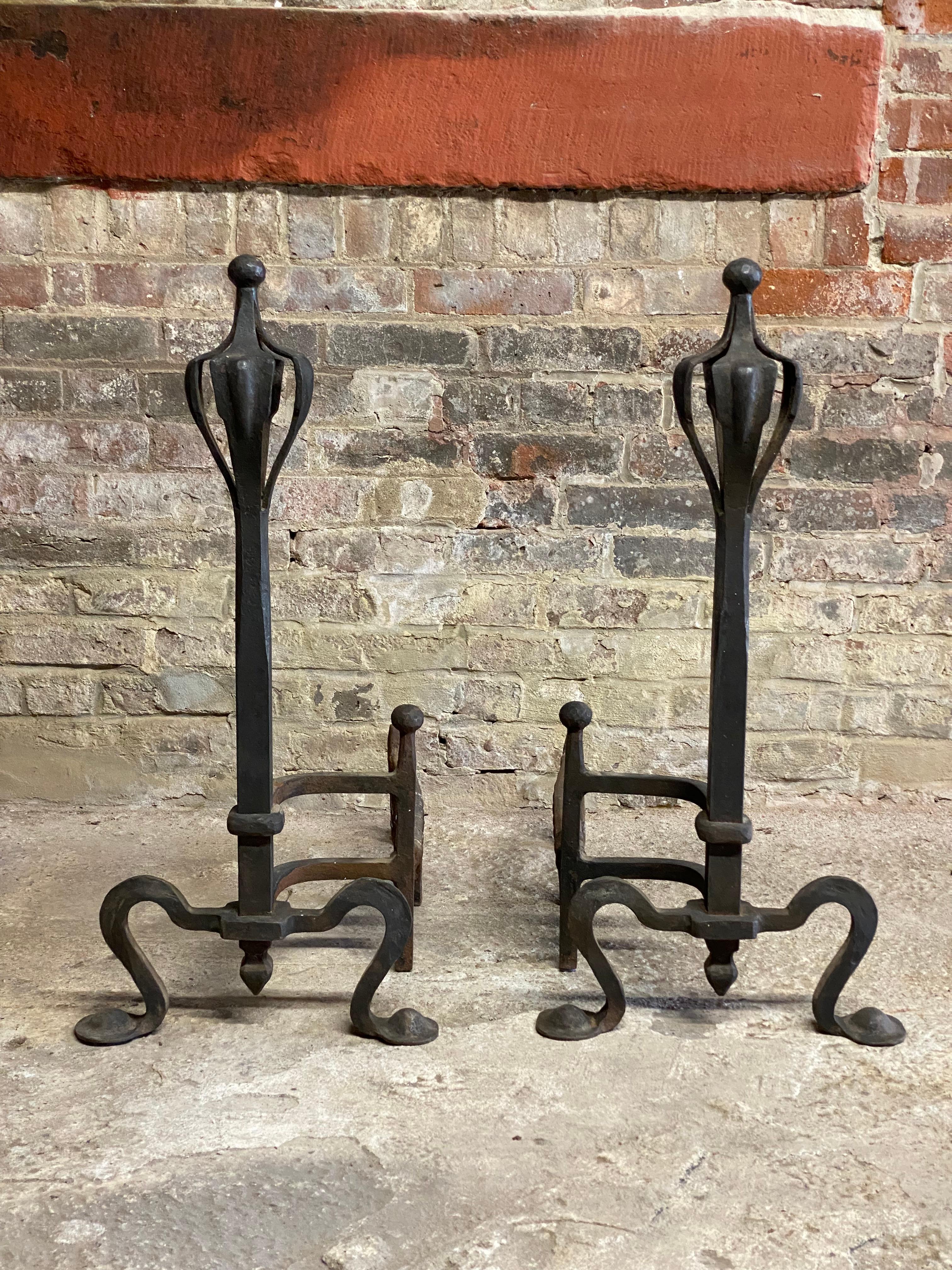 A monumental and impressive pair of American Arts and Crafts hand wrought andirons and fireplace tools. Dramatic scrolled leg with pad foot ending in an open 